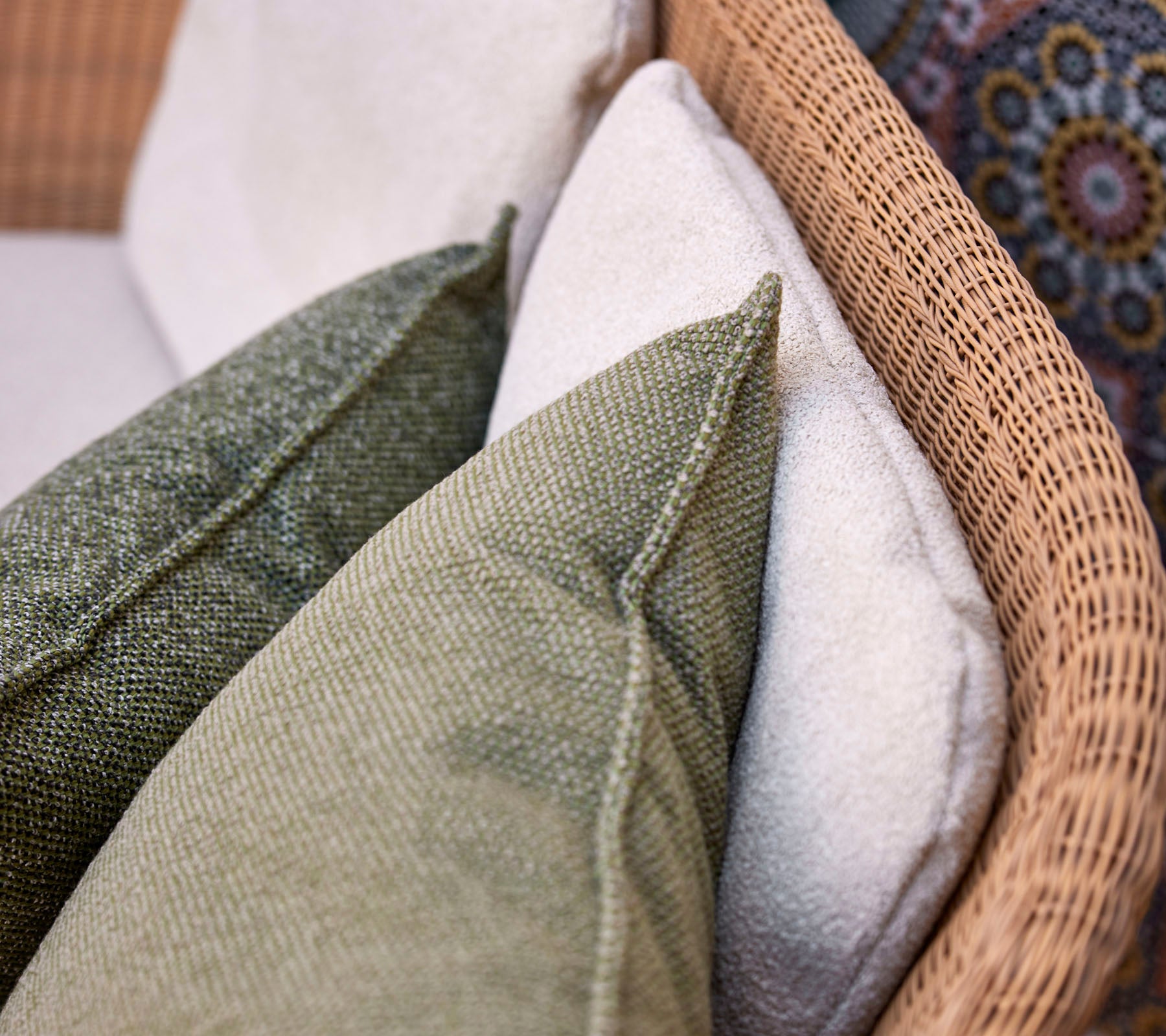 Un gros plan de coussins décoratifs dans diverses textures et couleurs, disposés sur une surface d'assise tissée.
