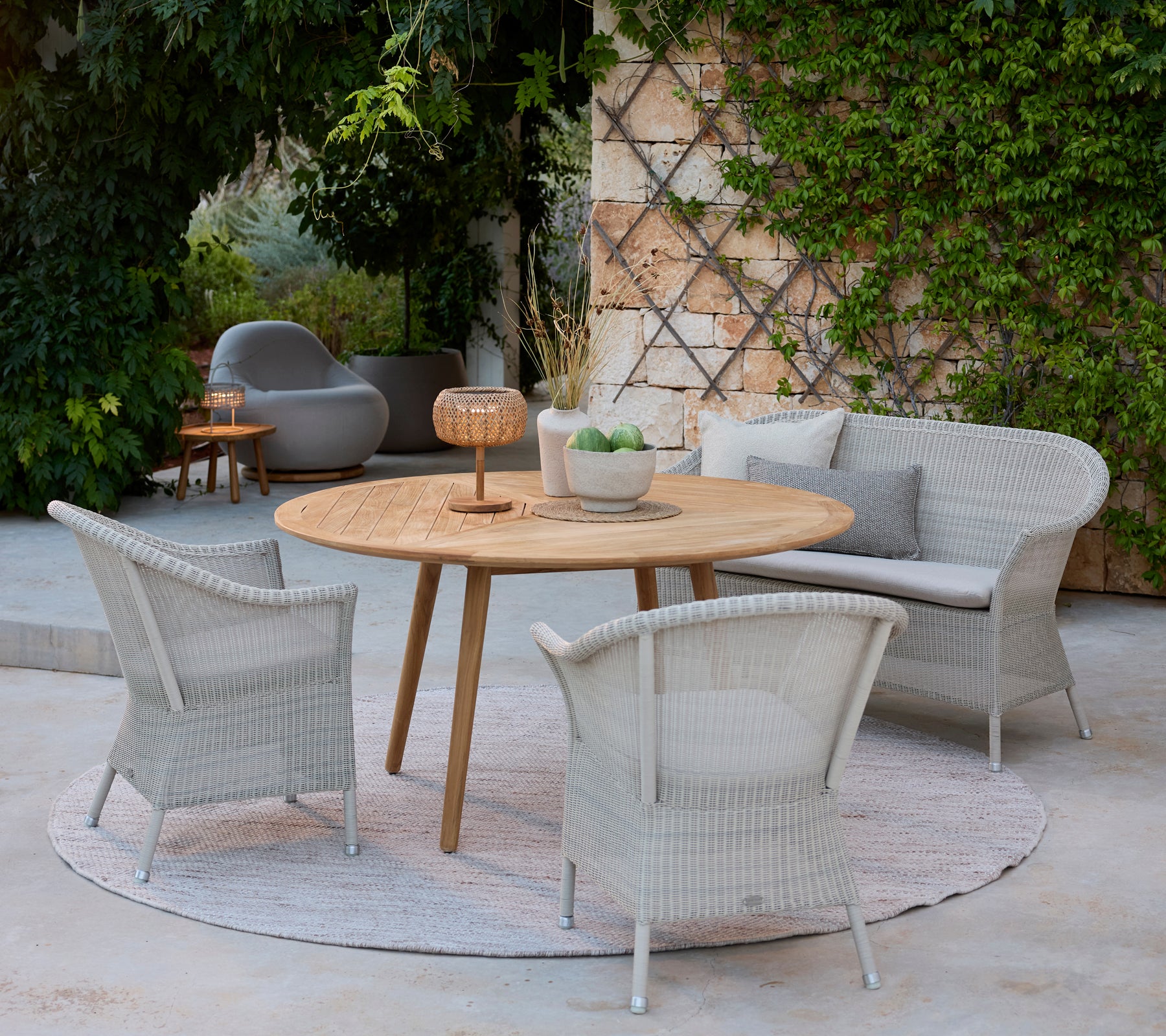 Espace salon moderne avec des chaises grises, une table ronde en bois et un canapé gris entouré de verdure.