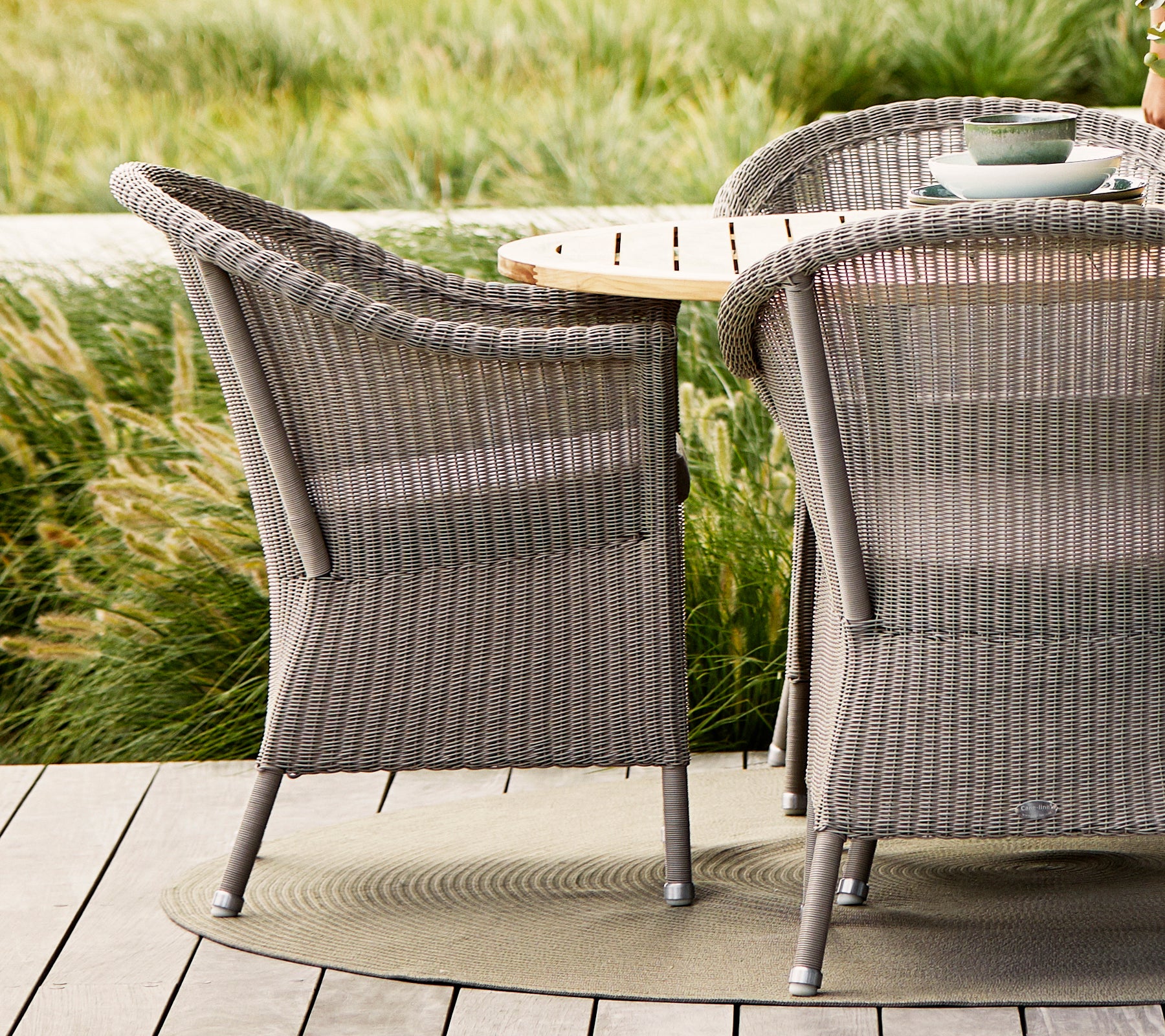 Chaises Taupe Lansing avec design tissé texturé, assorties à une table en bois naturel et entourées de verdure luxuriante.