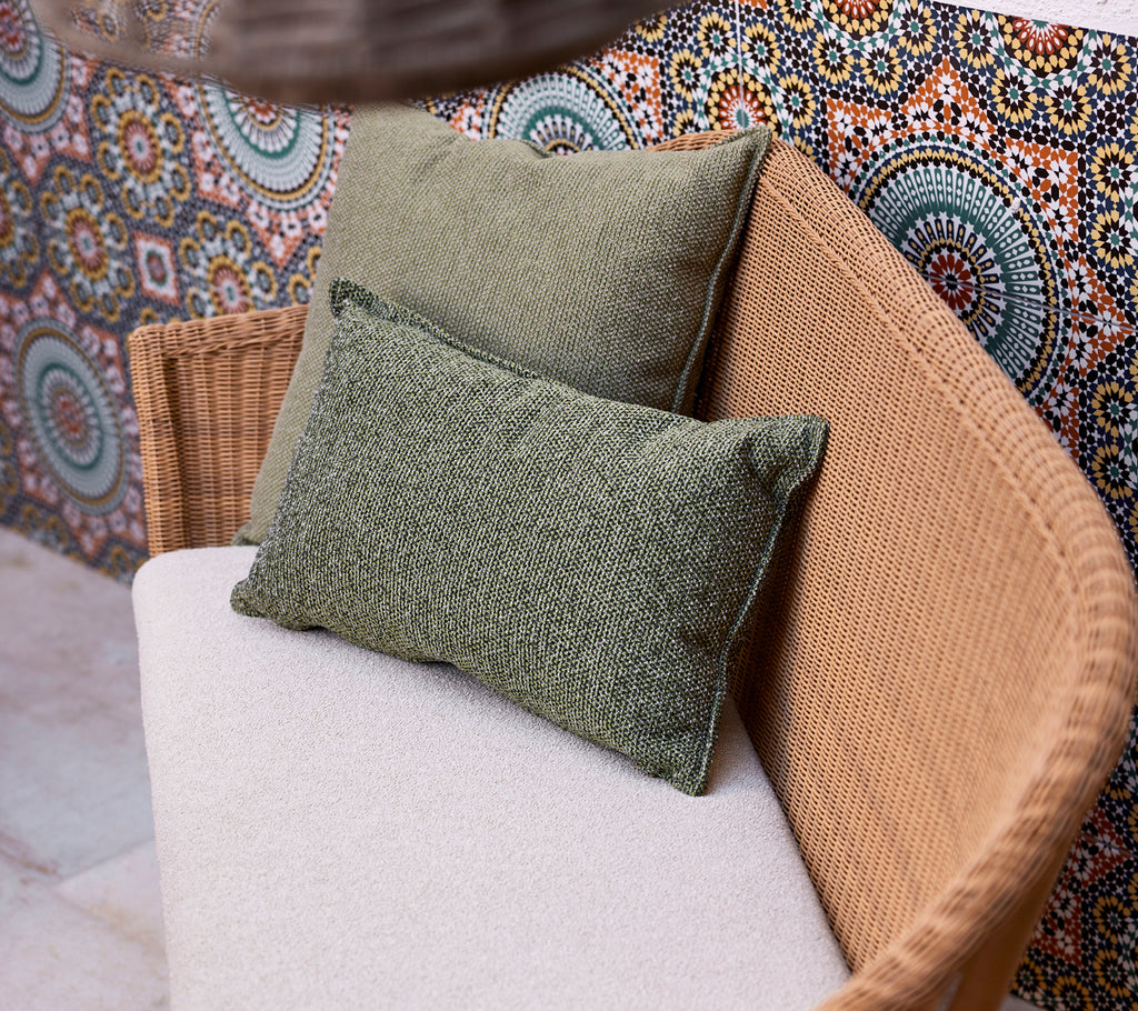 Deux coussins verts sur un canapé de couleur claire, positionnés contre un fond vibrant et à motifs comportant des designs circulaires.