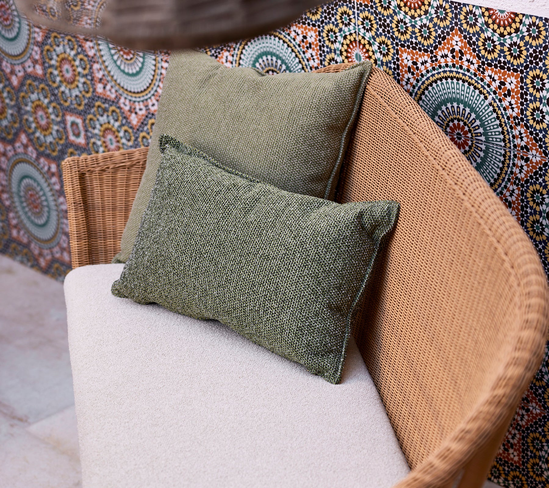 Deux coussins verts sur un canapé de couleur claire, positionnés contre un fond vibrant et à motifs comportant des designs circulaires.