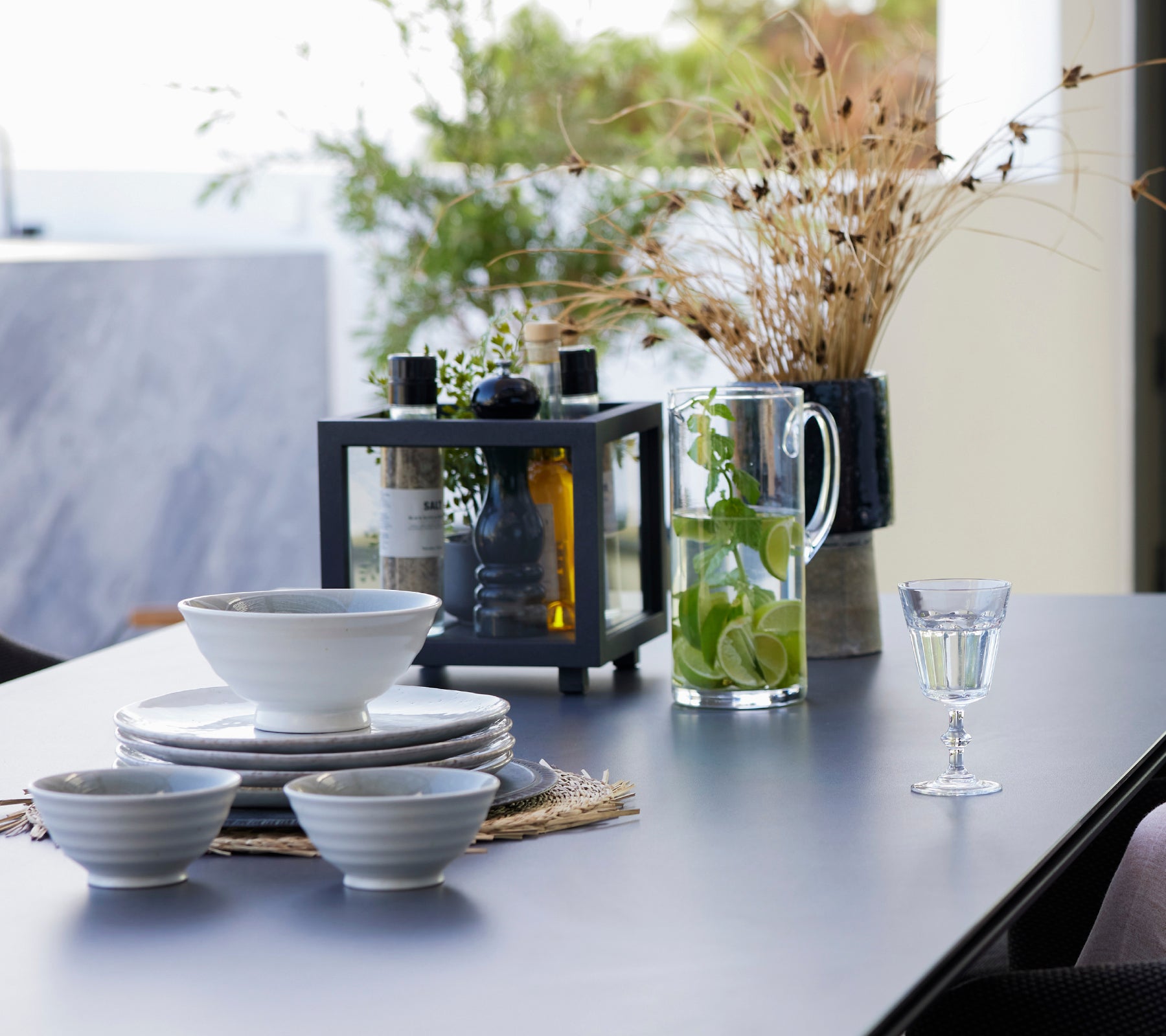 Table à manger dressé avec des bols blancs, une lanterne noire, une carafe en verre et des boissons.