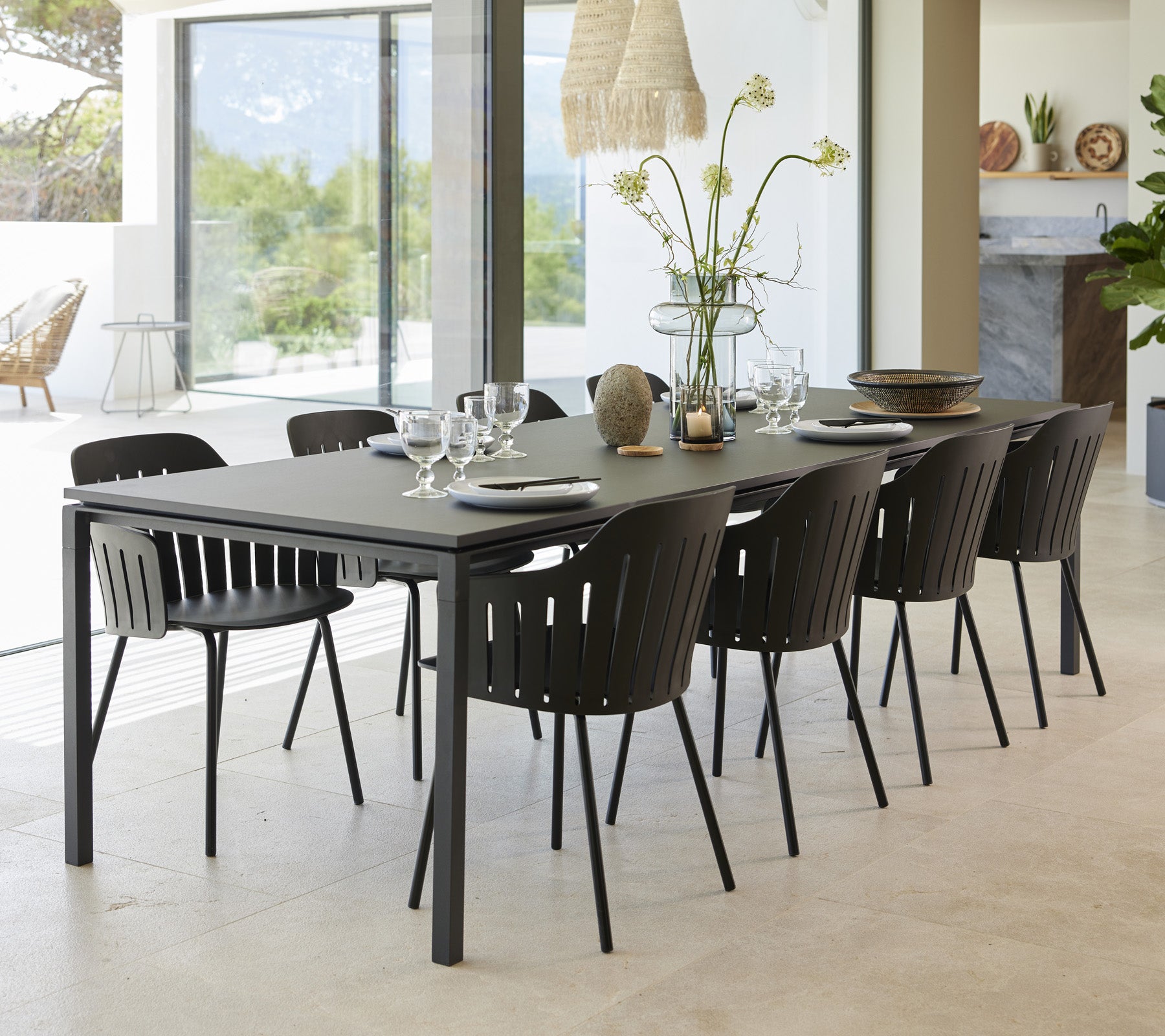Un ensemble de table à manger élégant avec huit chaises noires, disposé avec soin avec de la vaisselle et un vase de fleurs comme pièce maîtresse.