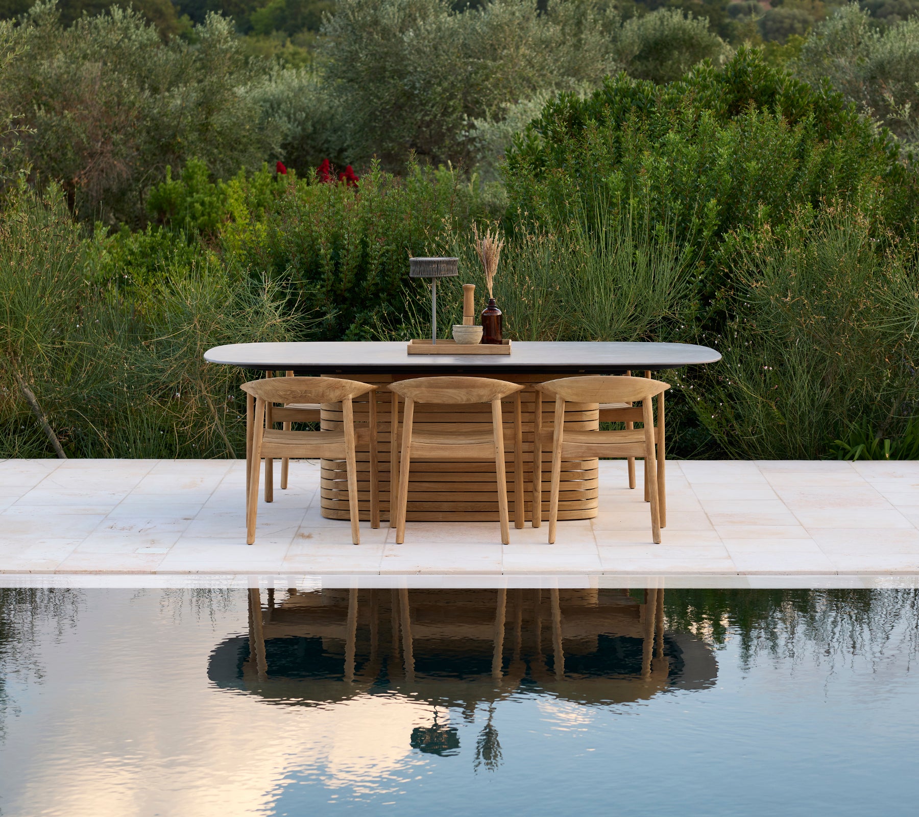 Table d'extérieur moderne avec des chaises près d'une piscine, entourée de verdure.
