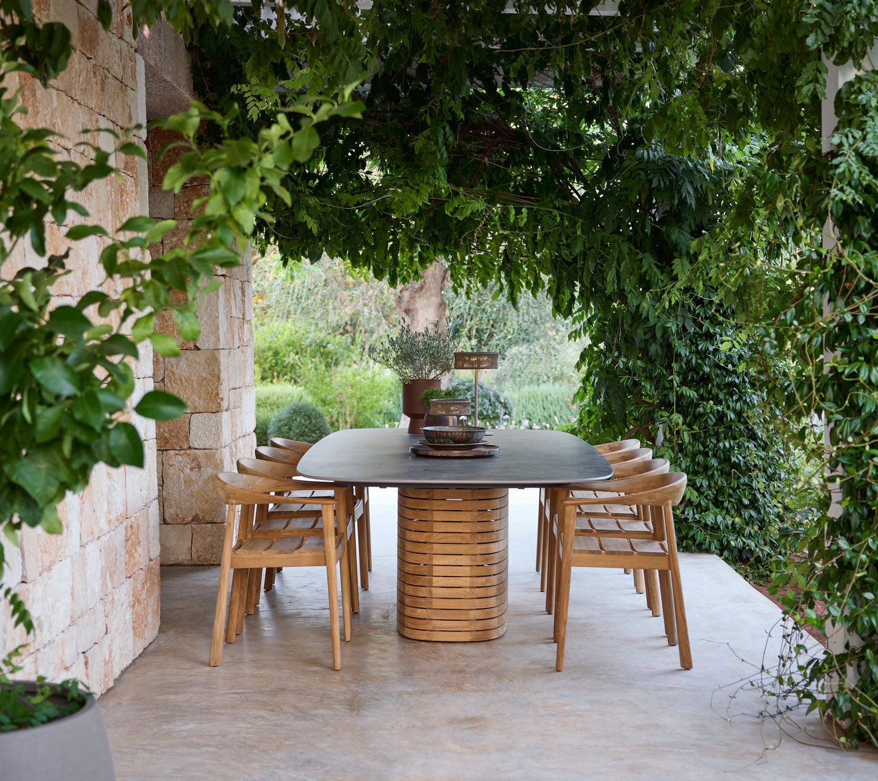 Table à manger en bois entourée de chaises sous la verdure.