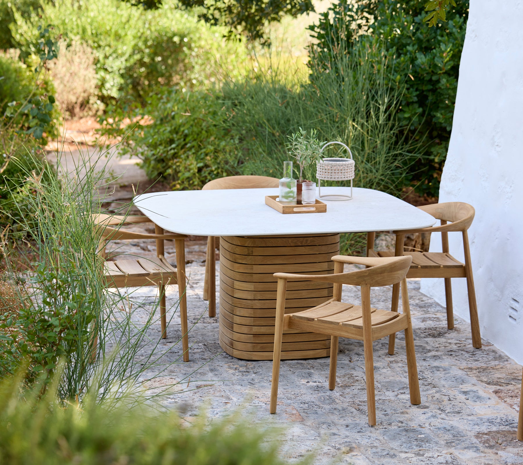 Cadre extérieur moderne avec une table blanche et des chaises en bois entourées de verdure.