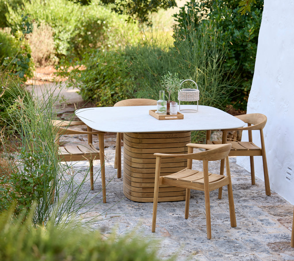 Cadre extérieur moderne avec une table blanche et des chaises en bois entourées de verdure.
