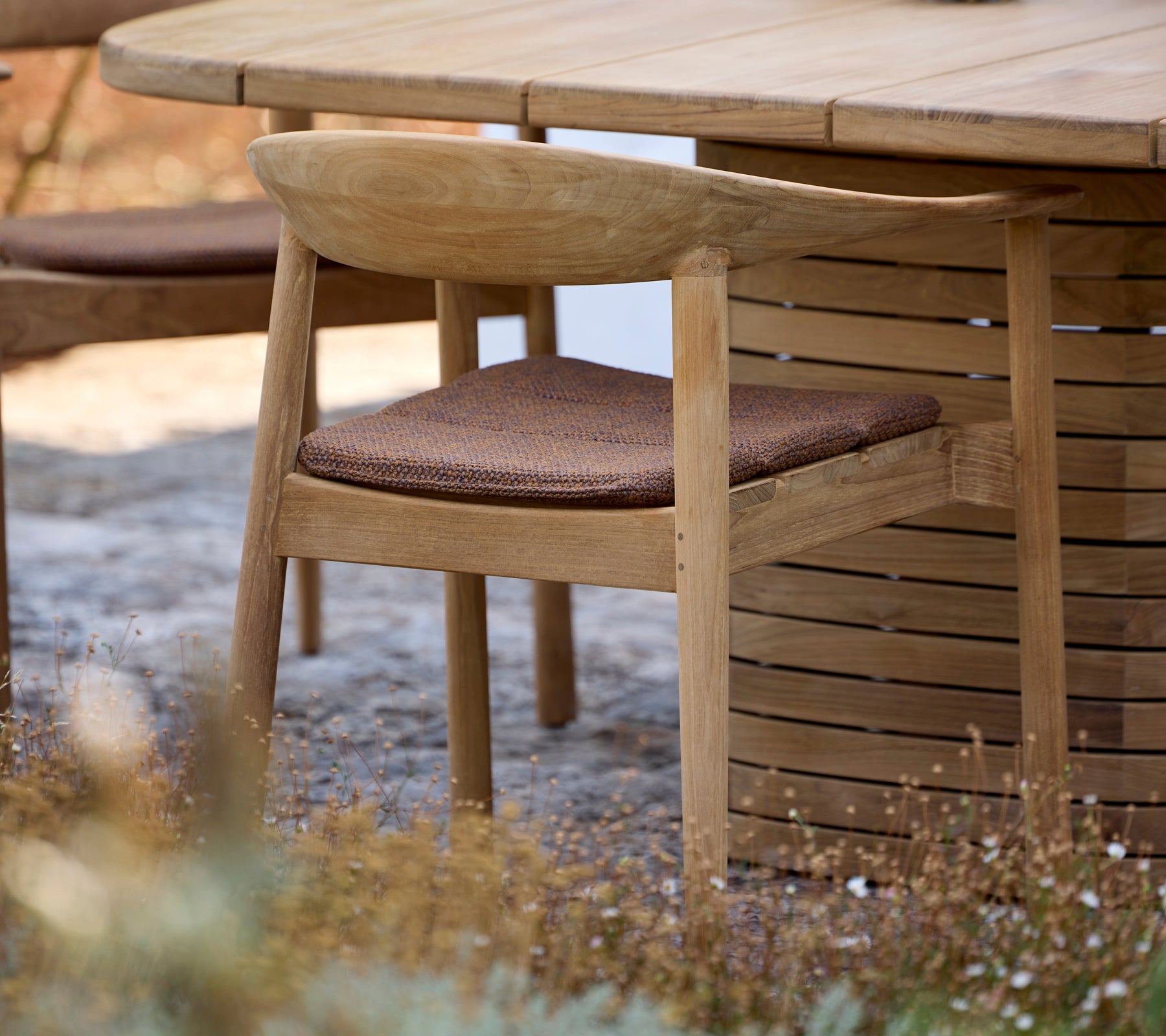 Chaise en bois avec coussin marron à côté d'une table ronde dans un cadre extérieur.