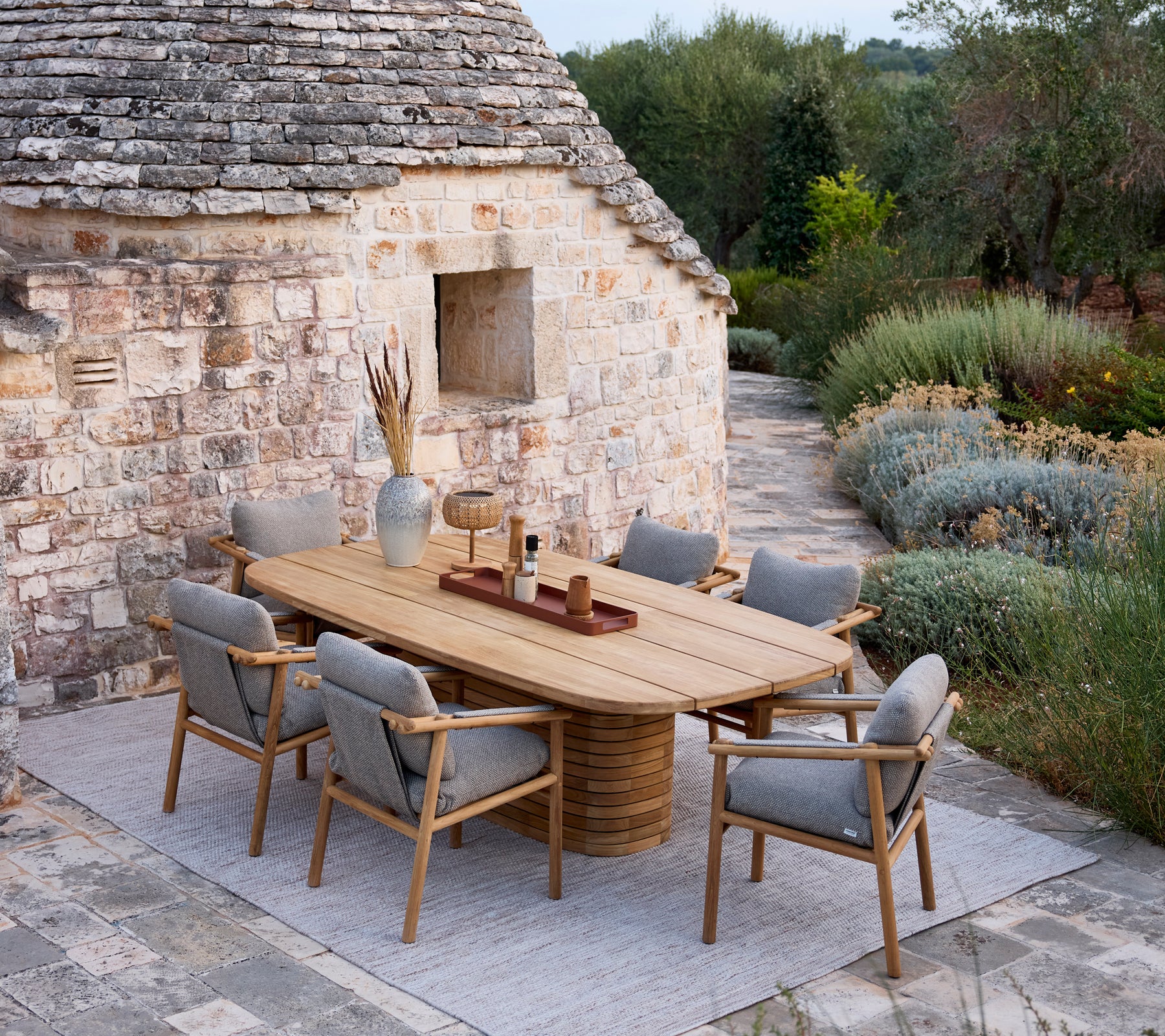 Table à manger en bois avec des chaises à coussin gris dans un cadre extérieur rustique.