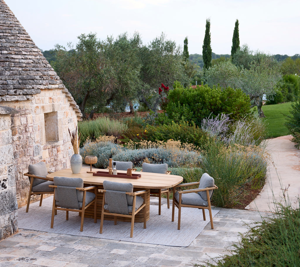 Installation moderne de repas en plein air avec une table ronde et des chaises grises entourées de verdure.