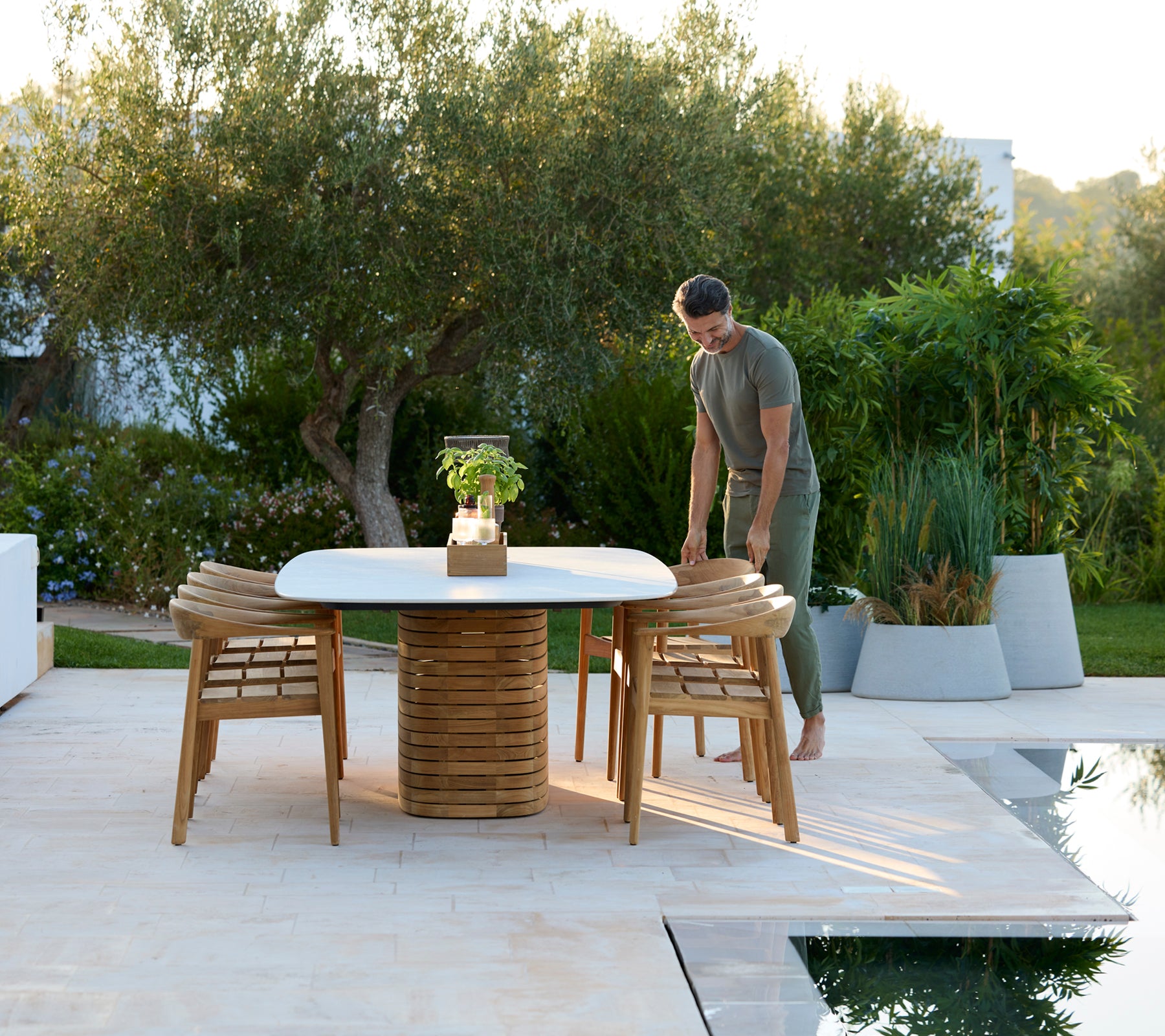 Table ronde moderne en extérieur avec des chaises en bois et de la verdure en arrière-plan.