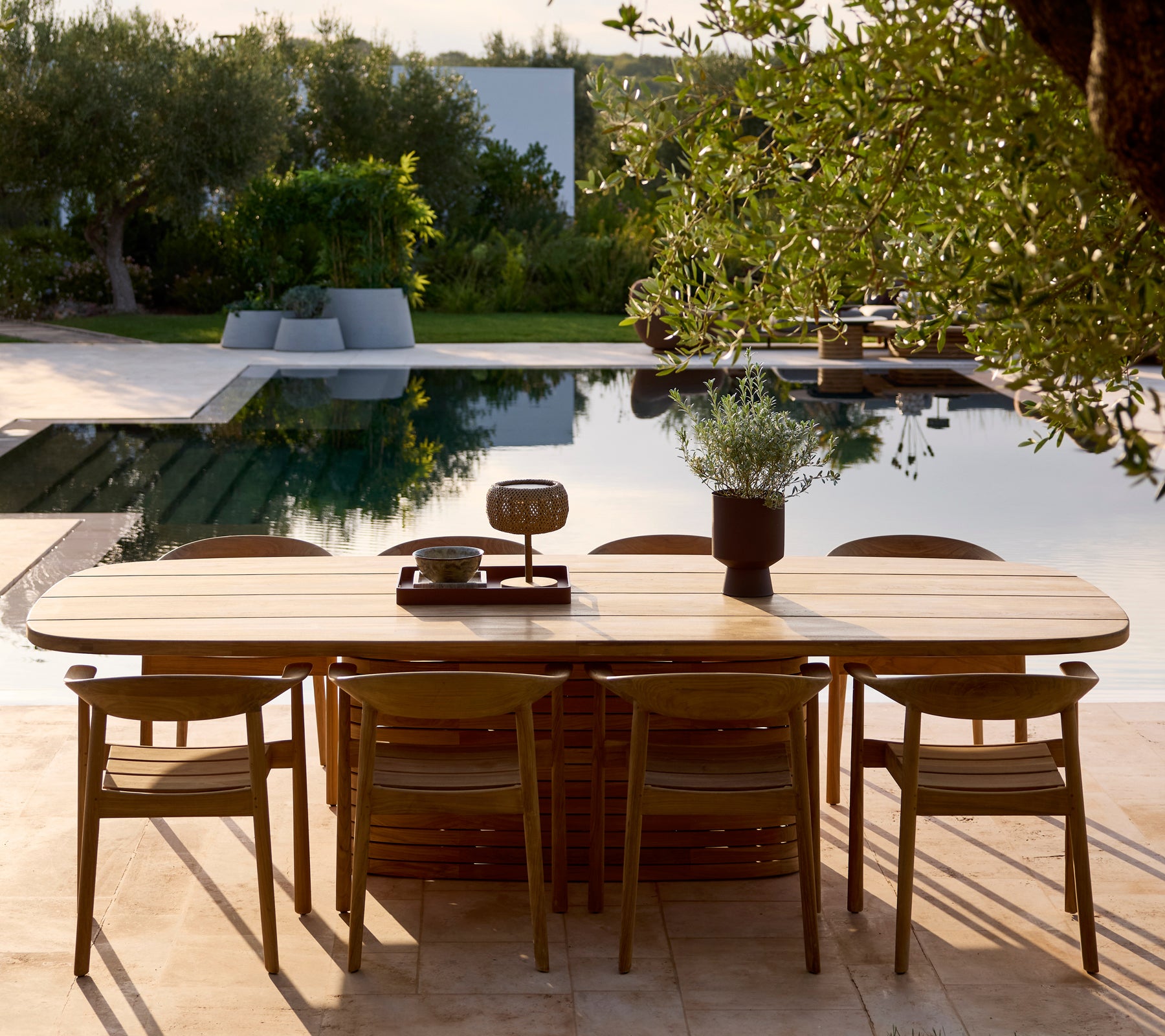 Ensemble de table en bois moderne et chaises près d'une piscine entourée de verdure.