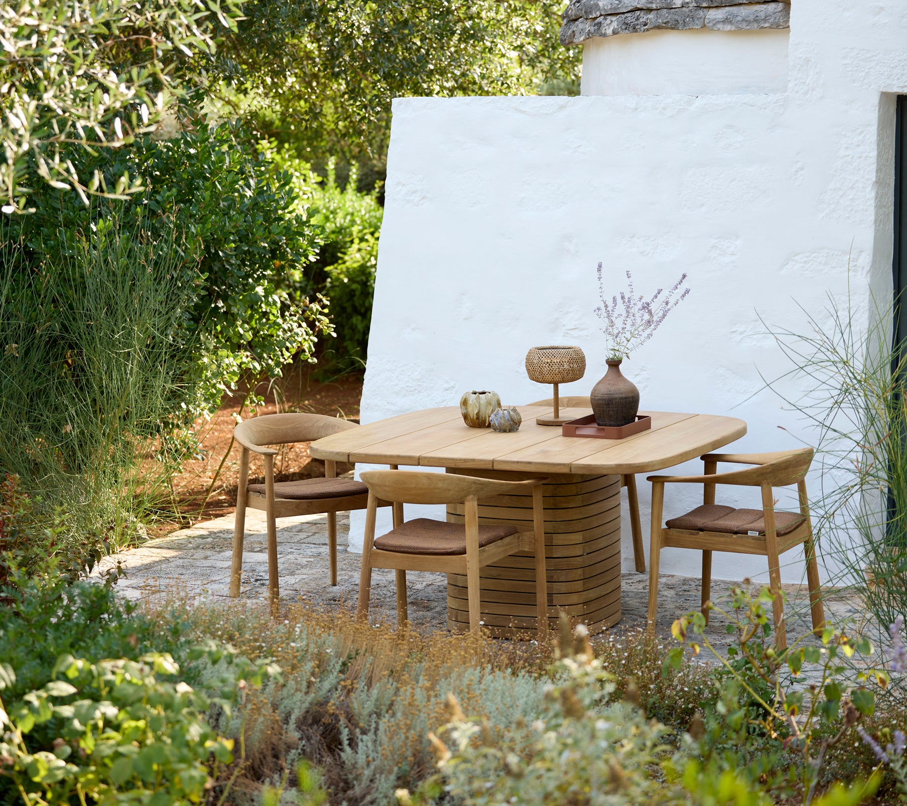 Table ronde moderne avec des chaises en bois et un vase décorative dans un cadre extérieur.