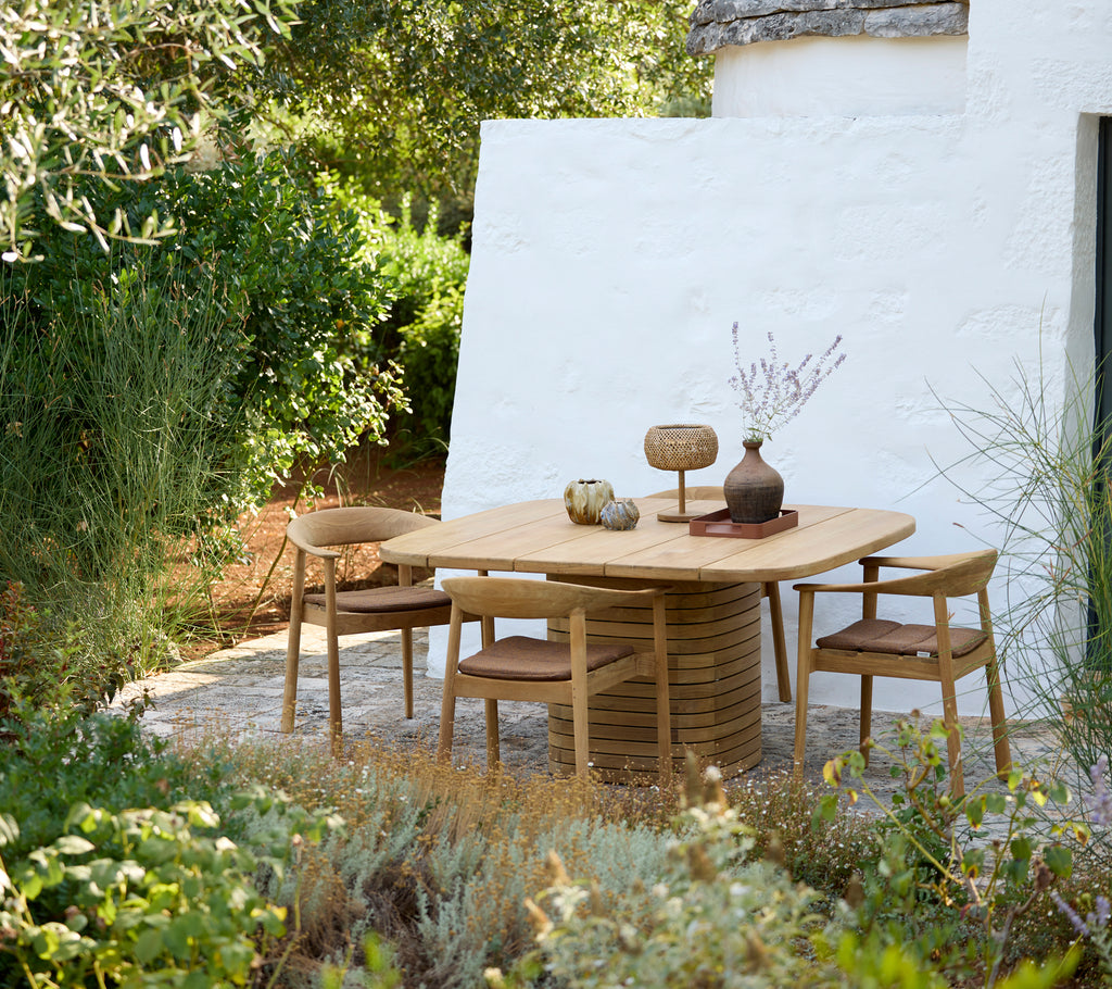 Table ronde moderne avec des chaises en bois et un vase décorative dans un cadre extérieur.