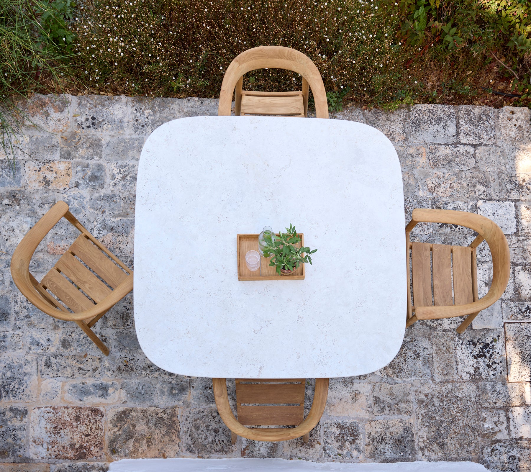 Table blanche moderne avec des chaises en bois et un petit centre de plante dans un cadre extérieur.