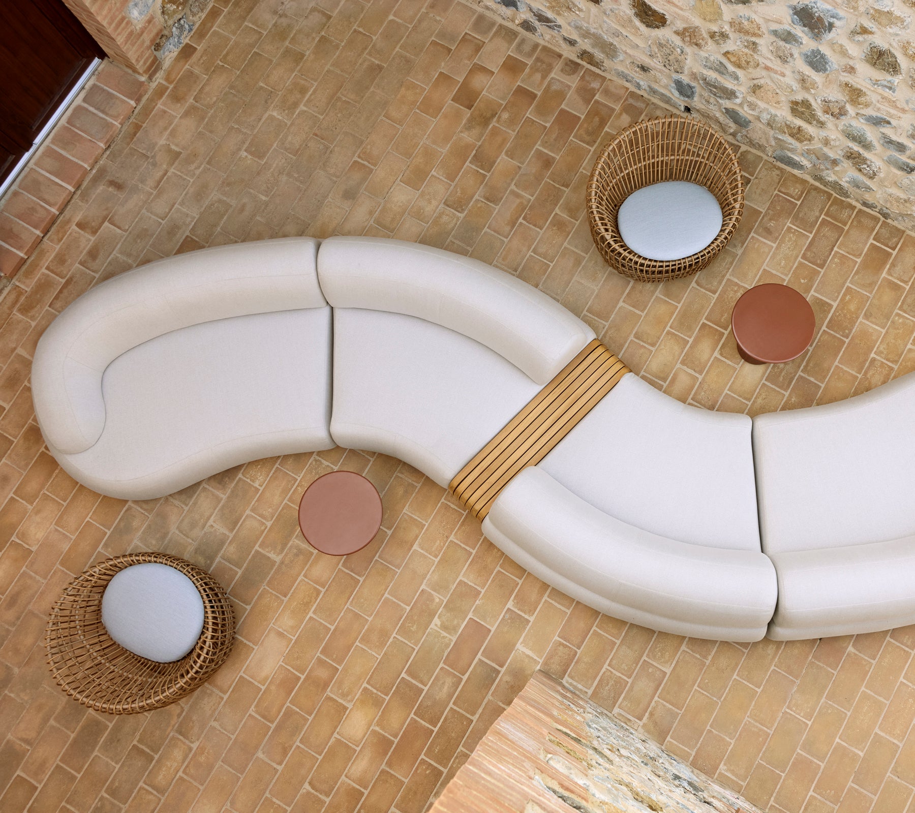 Salon apaisant avec un agencement de sièges blancs incurvés, deux tables basses Glaze rondes et des chaises Nest tissées sur un sol en pierre.