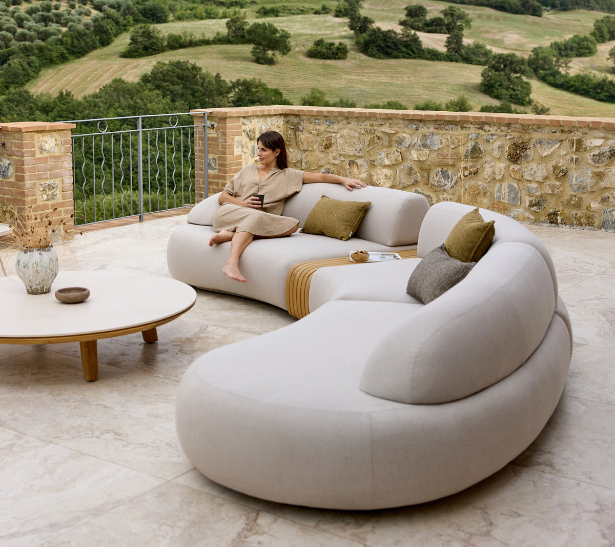 Un canapé lounge élégant aux courbes douces et aux coussins, complété par une table basse ronde, sur fond d'une vue pittoresque.