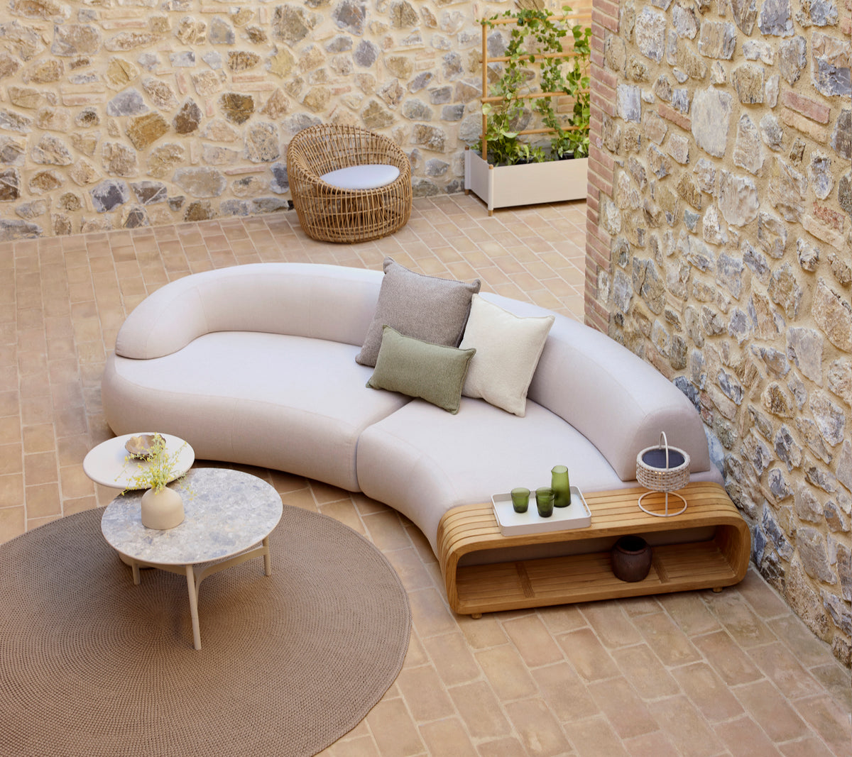 Canapé courbé et moelleux avec des coussins décoratifs, une table basse moelleuse et une chaise en nid ronde, placée sur un sol texturé.