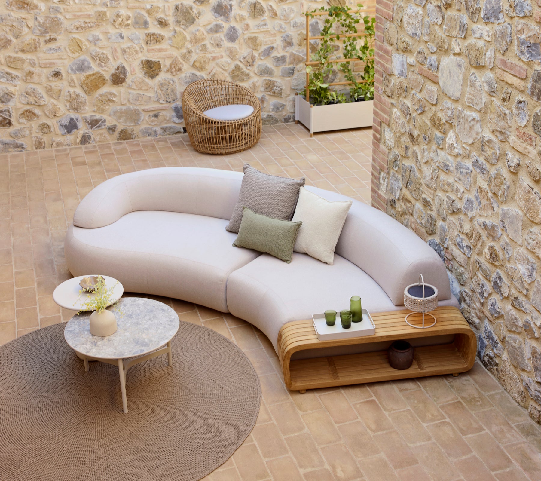 Canapé courbé et moelleux avec des coussins décoratifs, une table basse moelleuse et une chaise en nid ronde, placée sur un sol texturé.