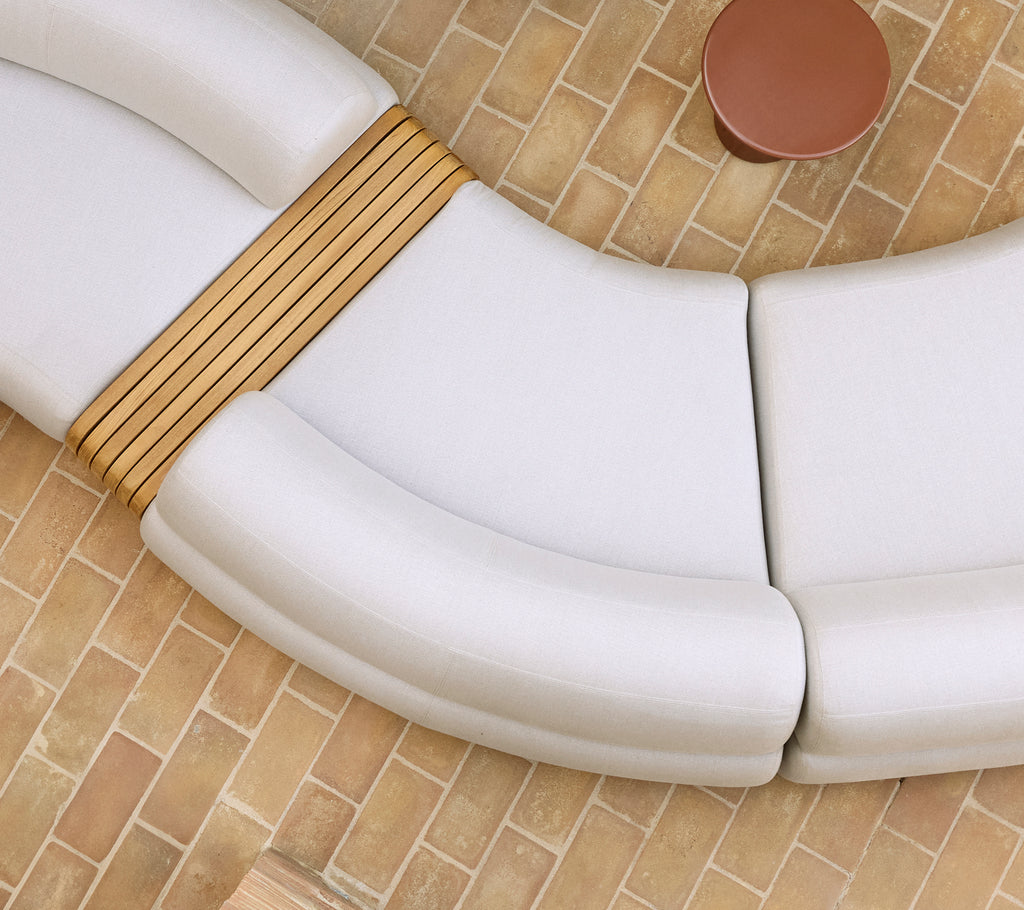 Module central de canapé doux aux courbes élégantes et accents en bois à côté d'une table basse ronde sur un sol texturé.