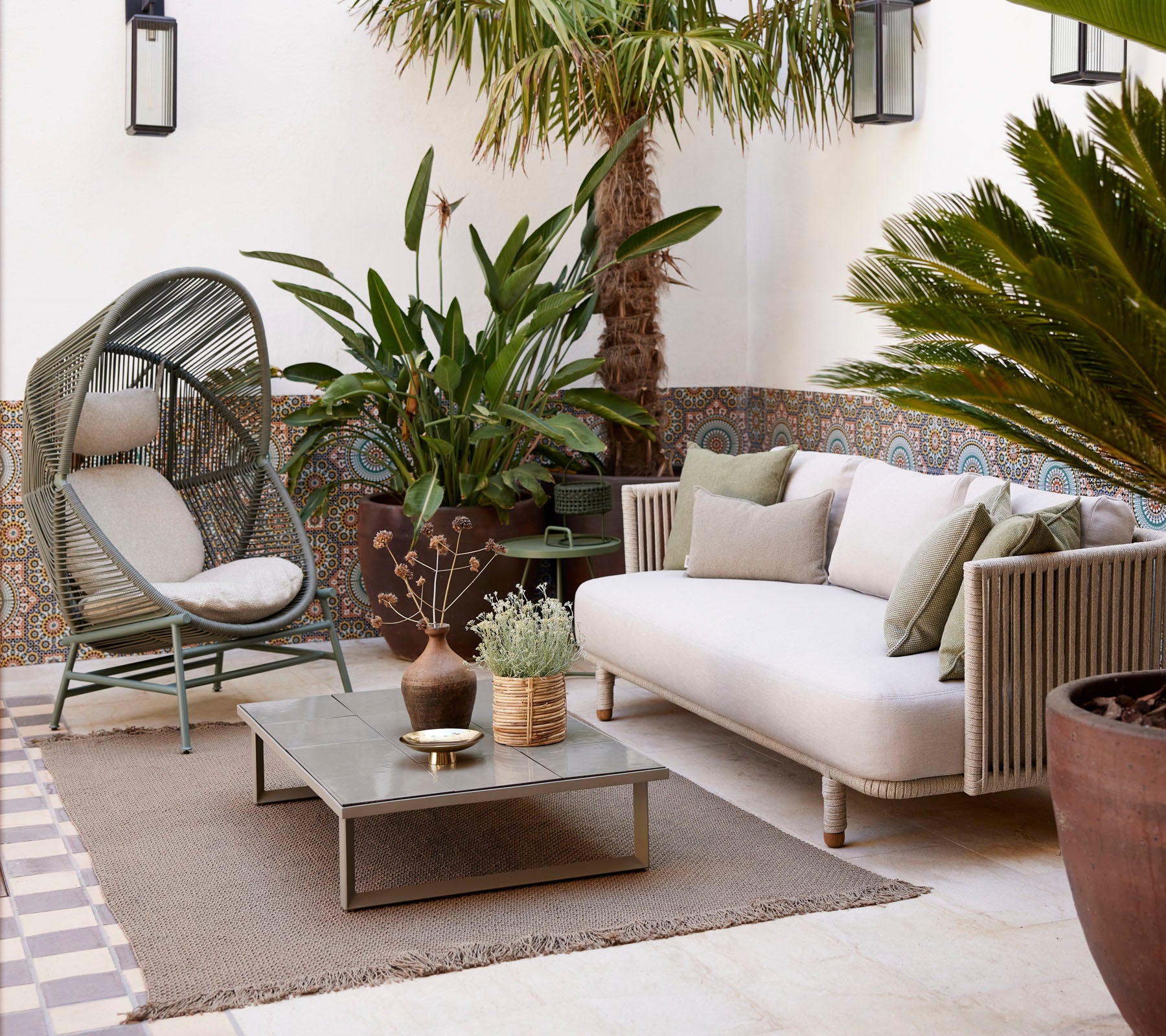 Espace de siège confortable avec des plantes, des tapis texturés et une table basse moderne, offrant une atmosphère sereine et accueillante.