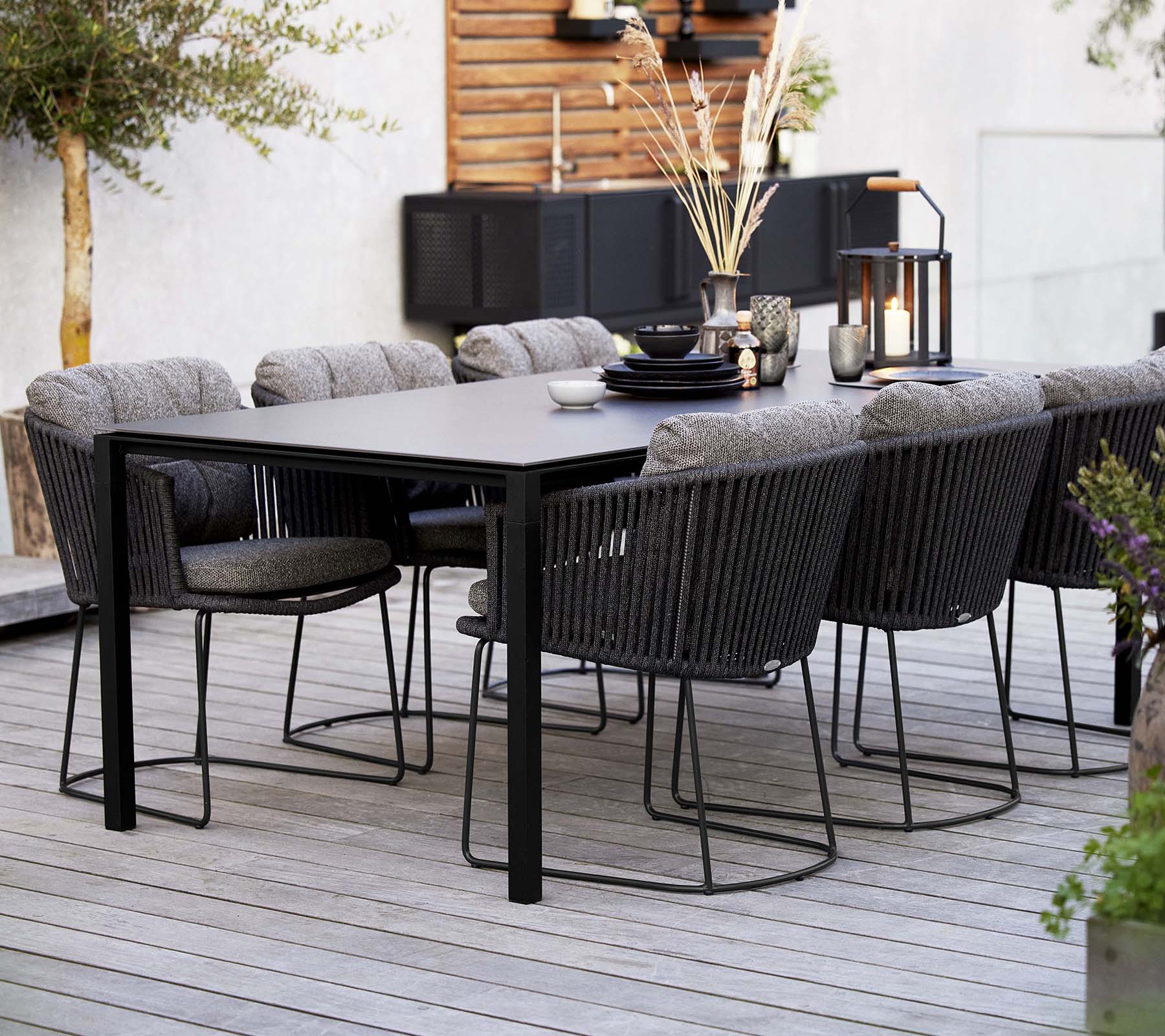Une installation de salle à manger élégante avec une table épurée entourée de chaises tissées confortables, ornée d'éléments décoratifs et de plantes.
