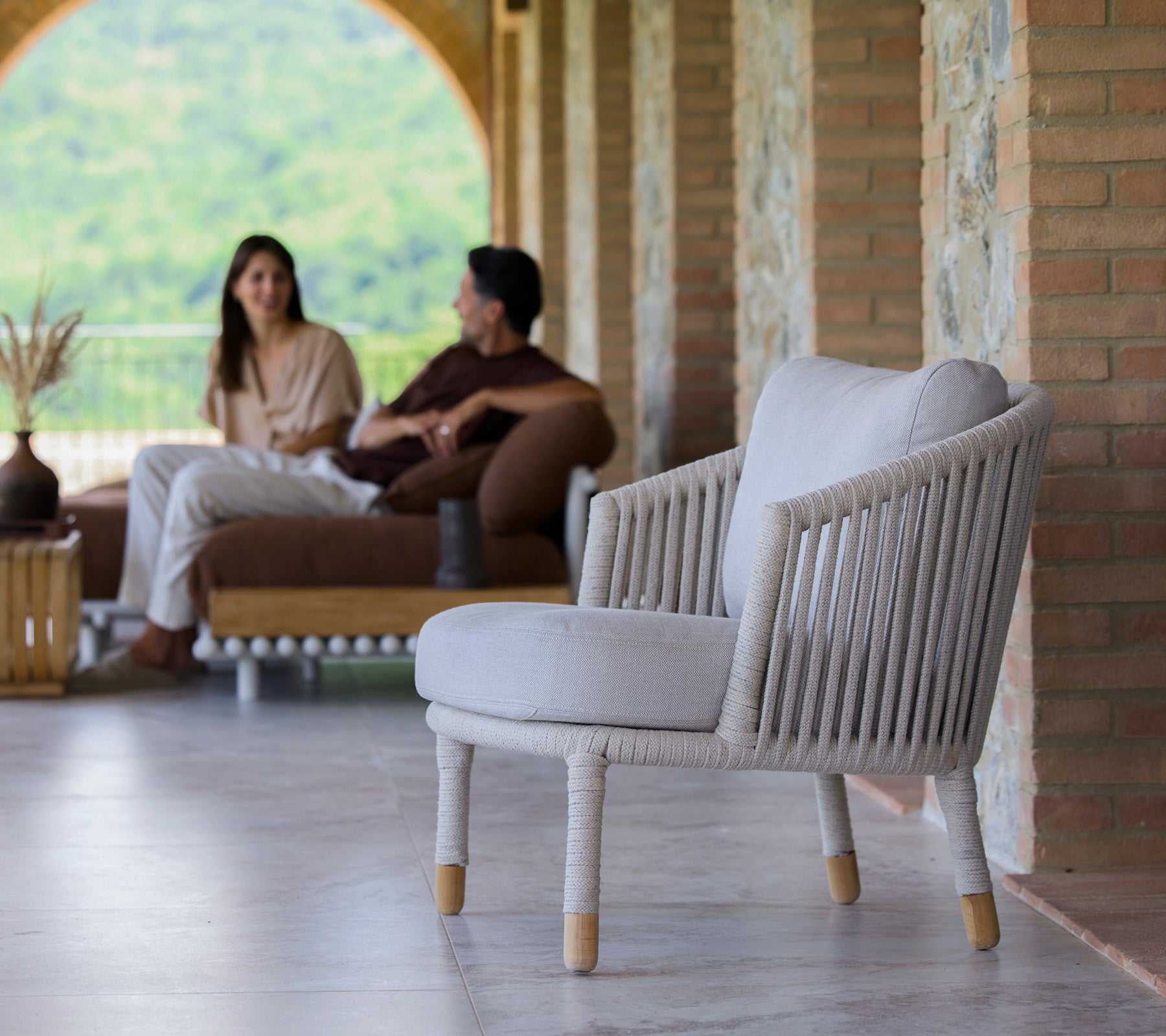 Une chaise longue couleur sable au design minimaliste, présentée dans un cadre serein avec des personnes engagées dans une conversation.