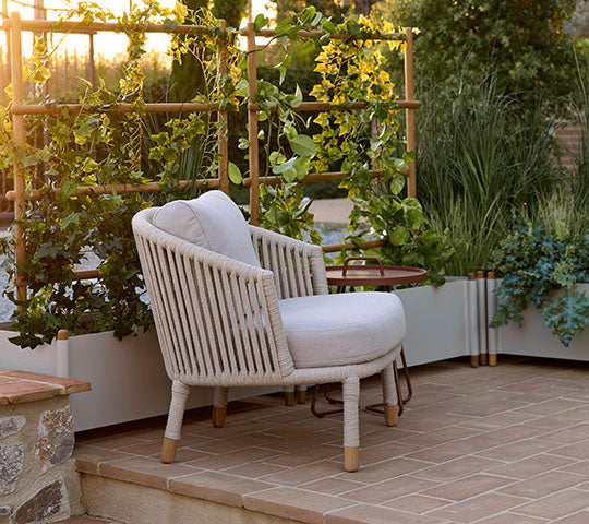 Chaise lounge Moments en couleur sable à côté d'un pot avec des plantes vertes, créant un coin salon cosy et accueillant.