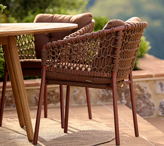 Une chaise rouge élégante avec des détails tissés à côté d'une table à manger en bois, complétant un cadre extérieur détendu.