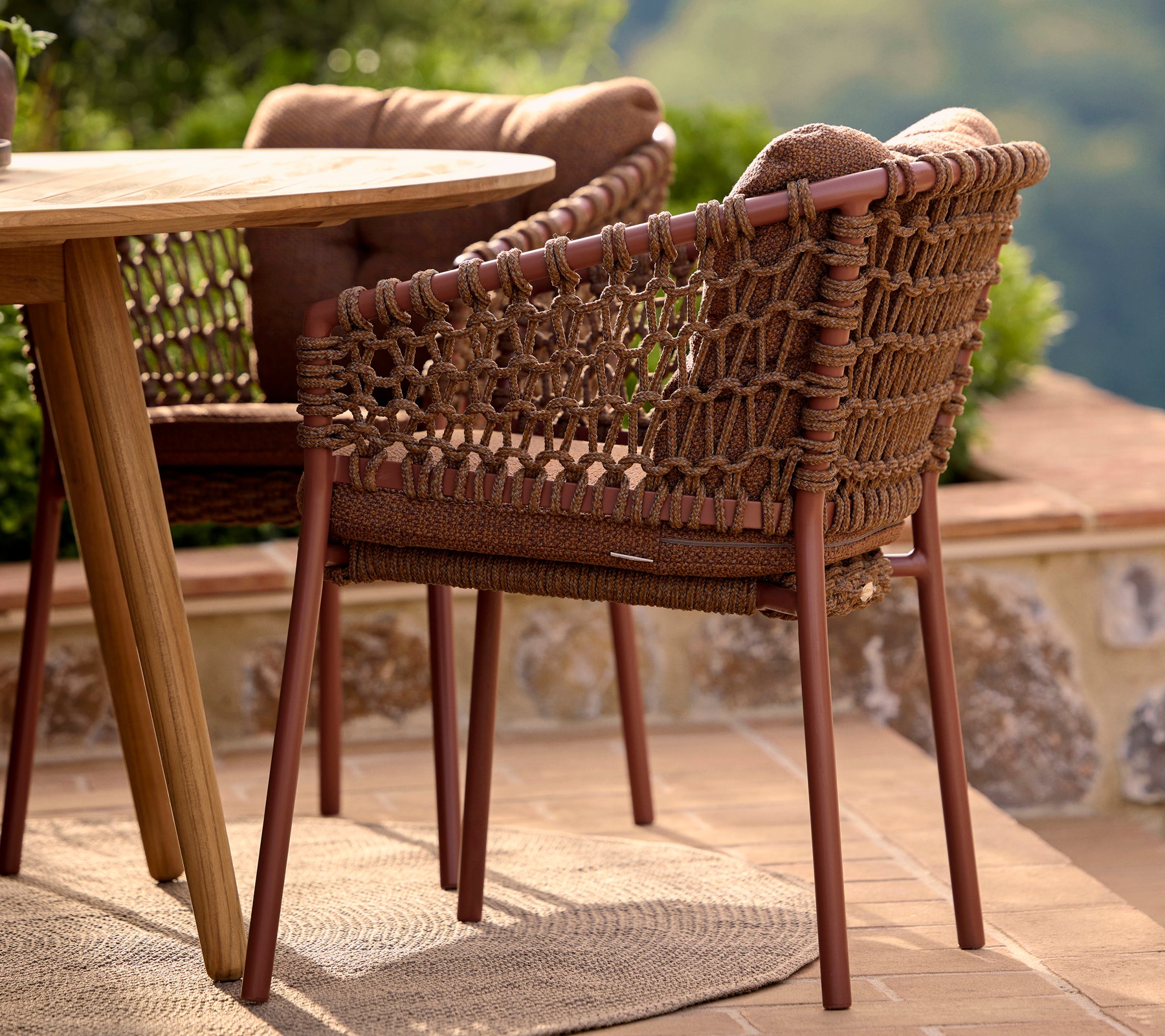 Chaise de salle à manger brun ombre avec un design tissé et des pieds solides, positionnée à côté d'une table ronde et entourée de verdure.