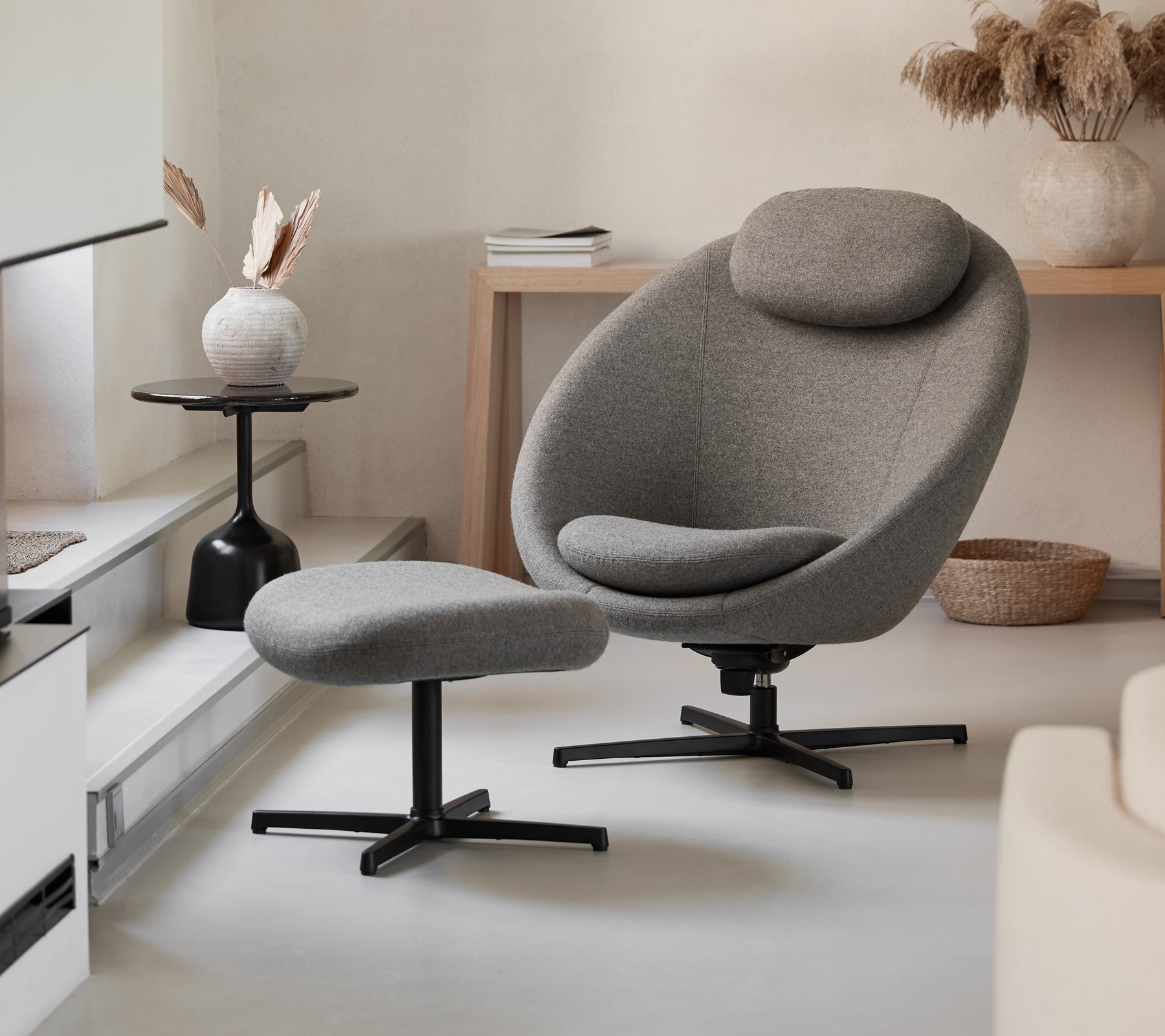 Chaise grise élégante avec ottoman assorti, présentant un design épuré et des courbes confortables, complété par des éléments de décoration modernes.