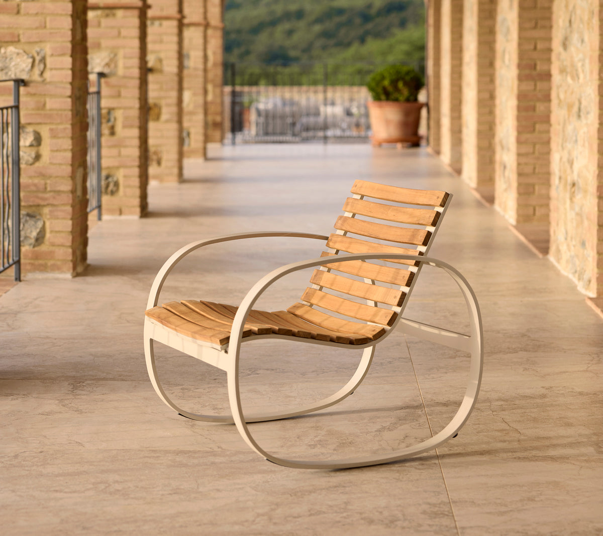 Fauteuil rocking Parc avec un cadre en aluminium et des lattes en bois, positionné sur un patio avec un sol en pierre et un cadre pittoresque.