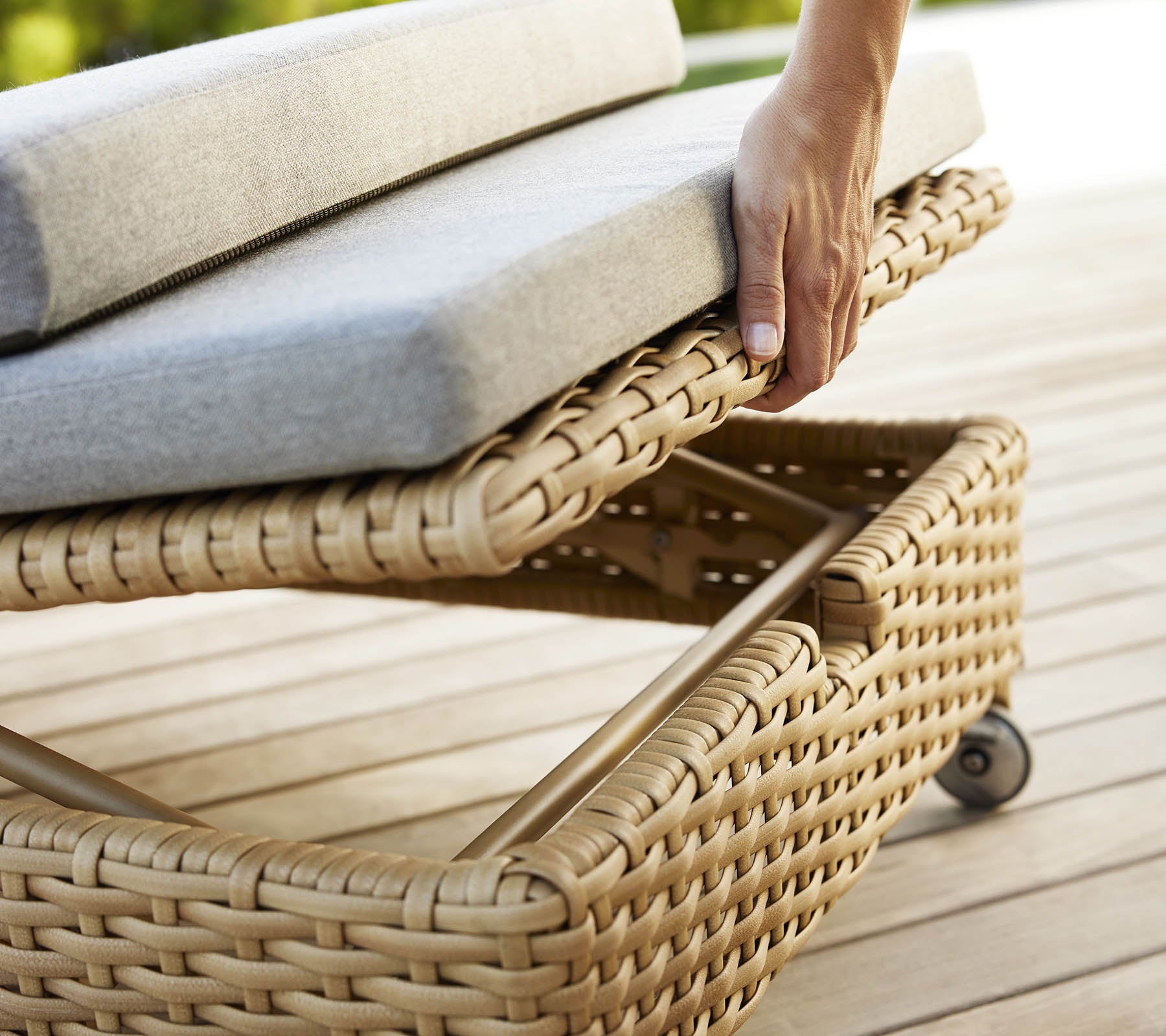 Une main ajuste le coussin d'un lit de repos tissé, au design élégant et à l'ameublement gris doux.