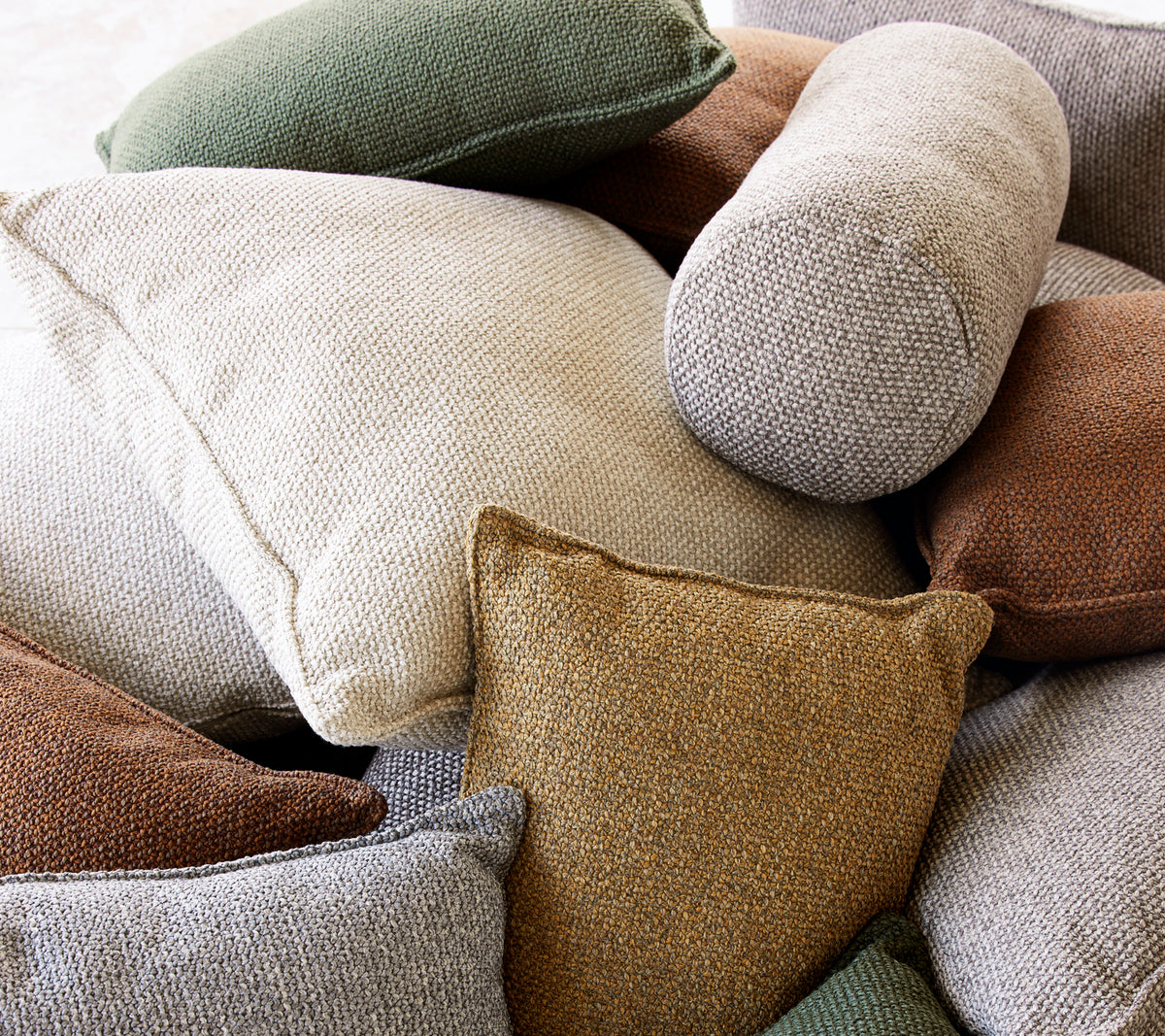 Une variété de coussins décoratifs texturés dans des tons neutres et des couleurs terre, présentant des formes et des tailles diverses.