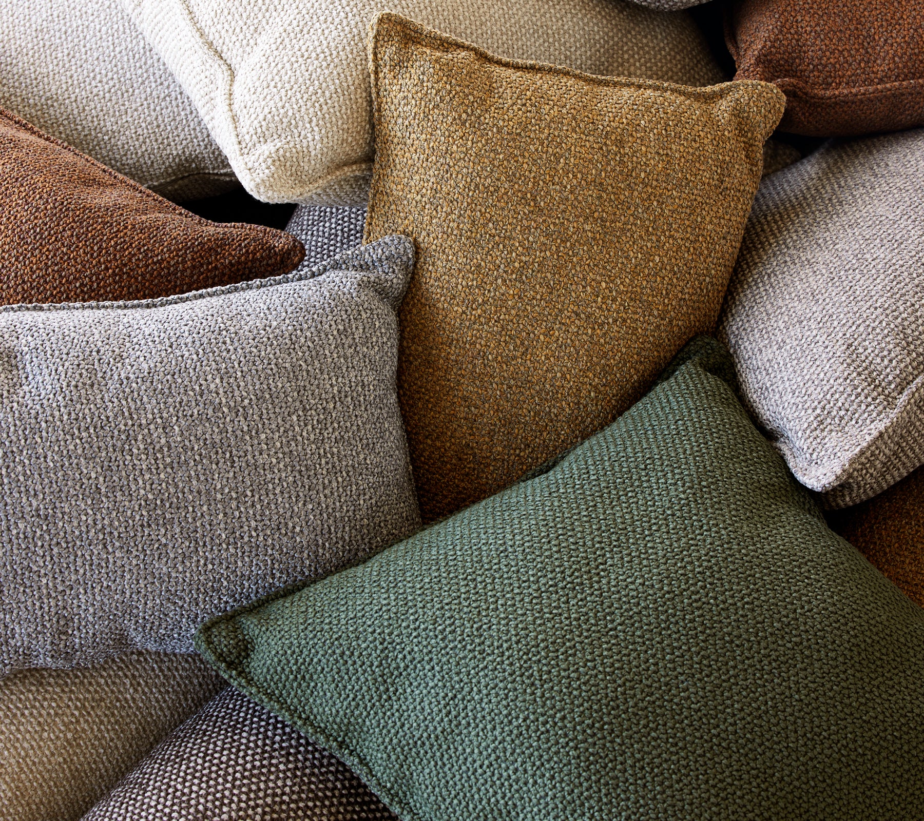 Une collection de coussins texturés dans diverses couleurs, y compris vert, brun et crème, empilés ensemble.