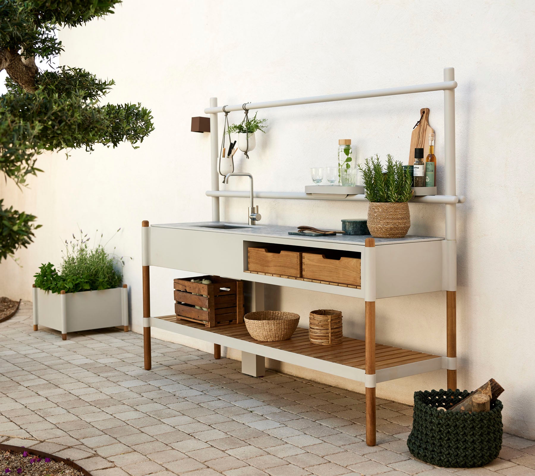Unité de cuisine moderne avec un évier en métal, des étagères en bois et des plantes décoratives dans des conteneurs élégants. Design épuré avec des éléments naturels.