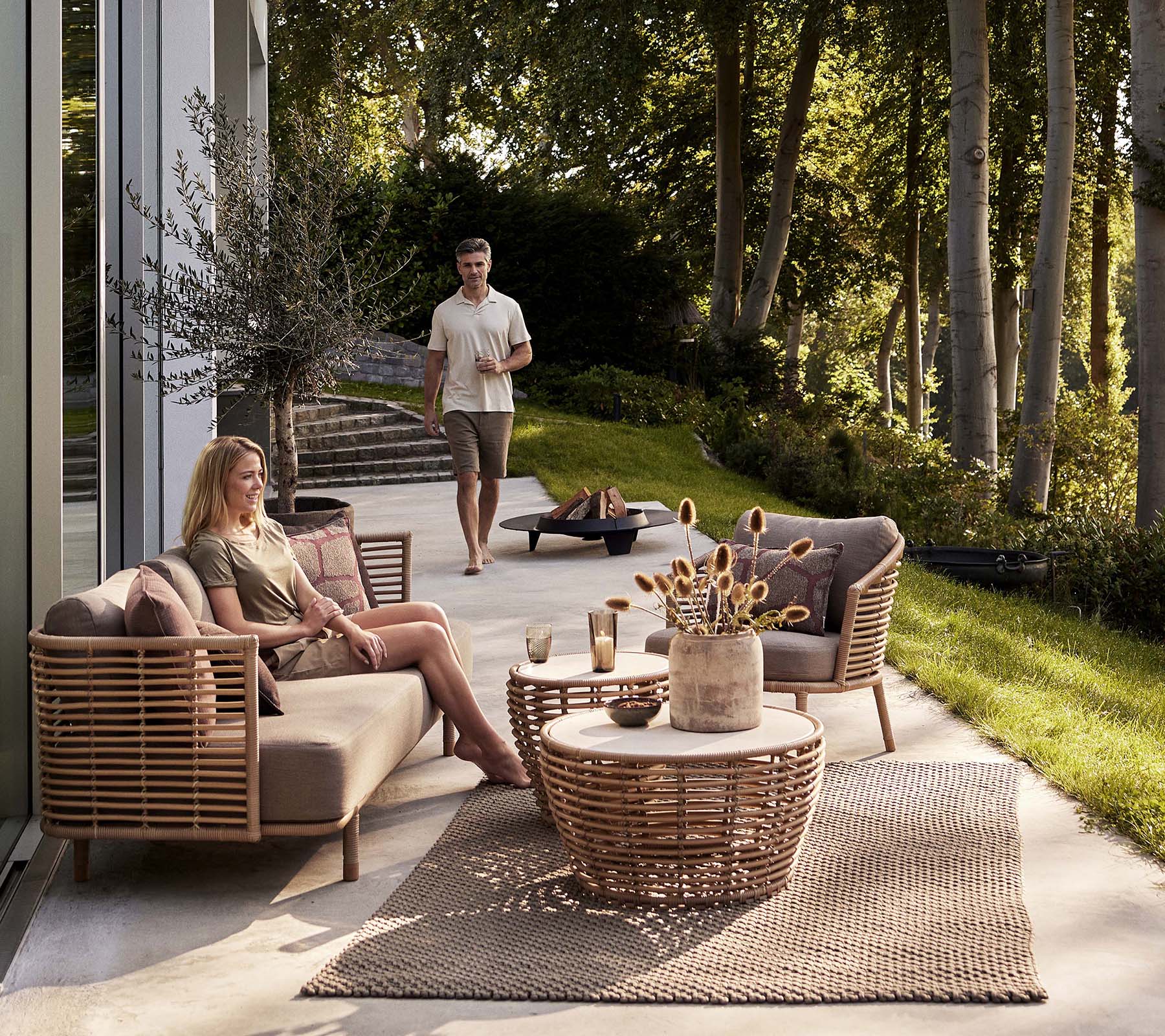 Un aménagement de sièges cosy avec un canapé Sense et un fauteuil, accompagné d'une table basse en osier et d'éléments décoratifs.