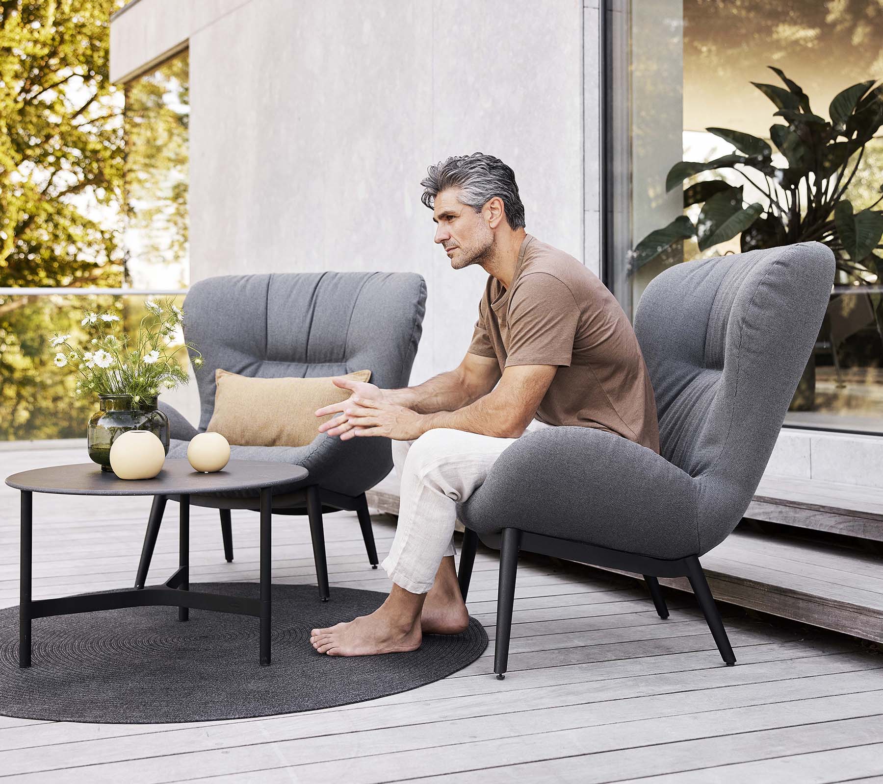 Un fauteuil lounge serein avec un homme assis, une petite table à proximité et des objets décoratifs, créant une atmosphère détendue.