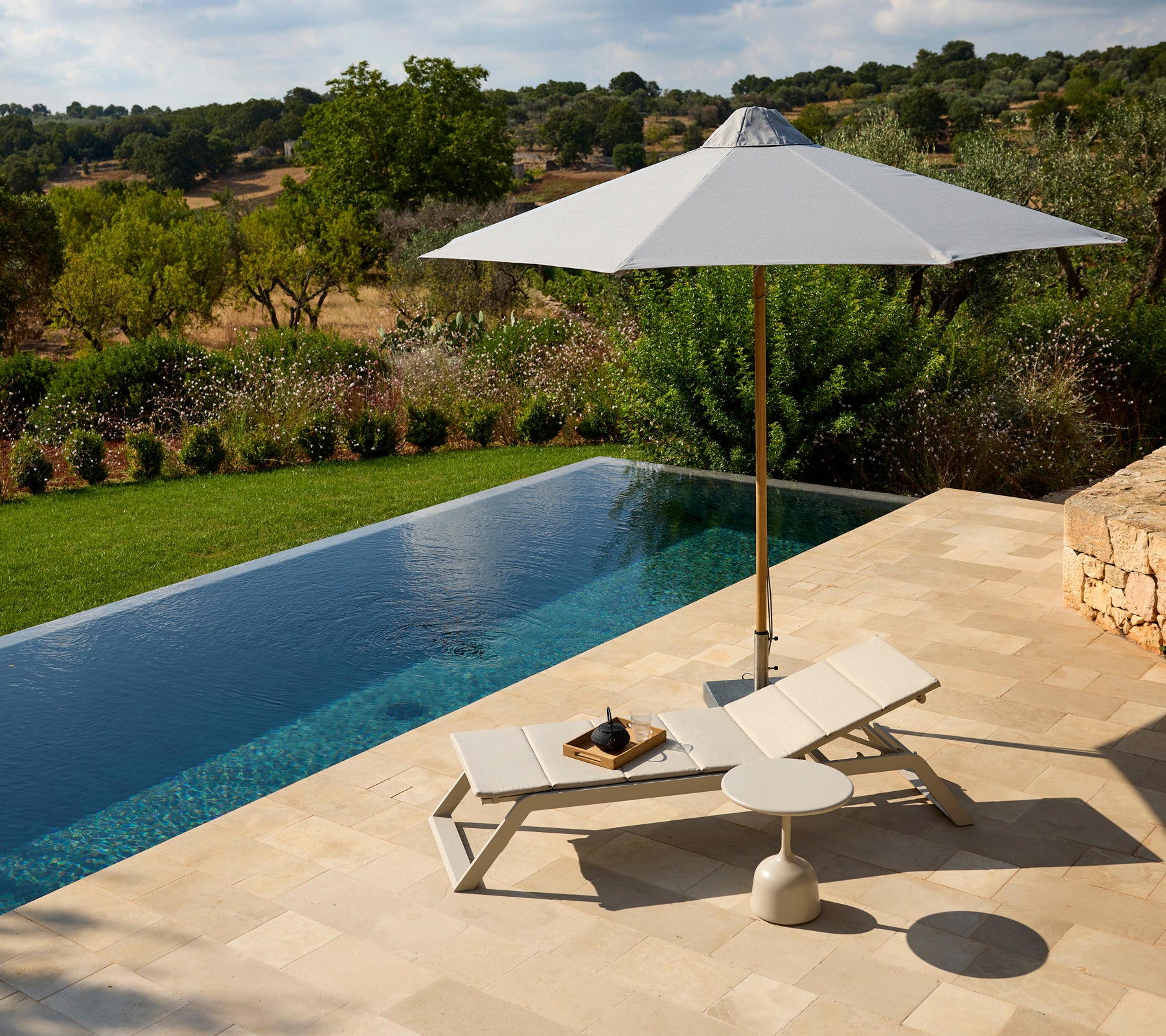Espace lounge moderne en plein air avec une chaise blanche, un parasol et une table d'appoint près d'une piscine.