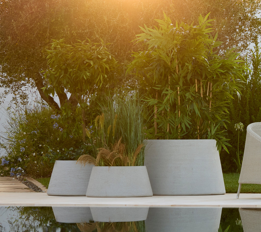 Collection de pots gris disposés dans un décor de jardin avec une verdure luxuriante.