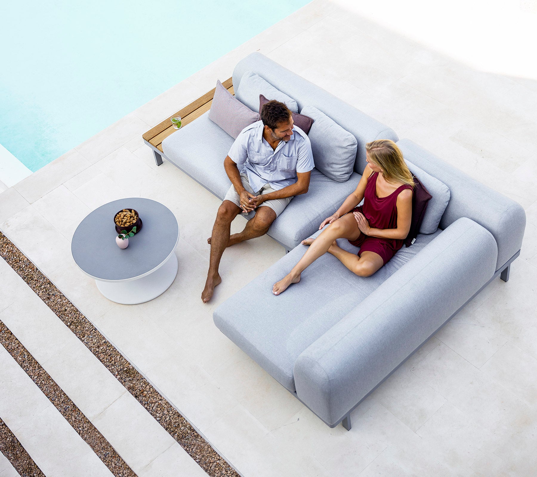 Un homme et une femme sont assis sur un canapé gris moderne, engagés dans une conversation, avec une petite table et des objets décoratifs à proximité.
