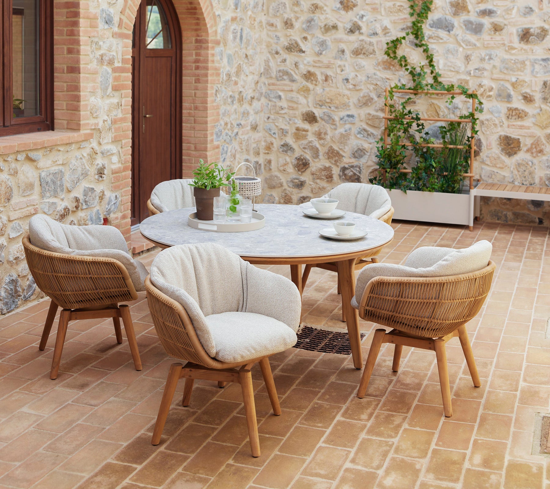 Une installation de salle à manger élégante avec une table ronde entourée de chaises pivotantes avec des pieds en teck et des coussins confortables, complétée par de la verdure.