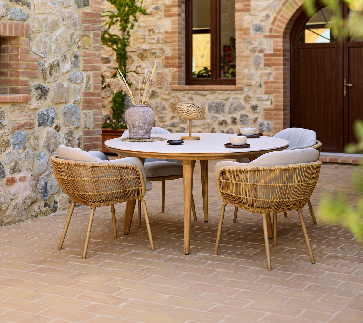 Aménagement de repas en extérieur avec une table Aspect ronde et des chaises Stay, le tout devant un mur en pierre.