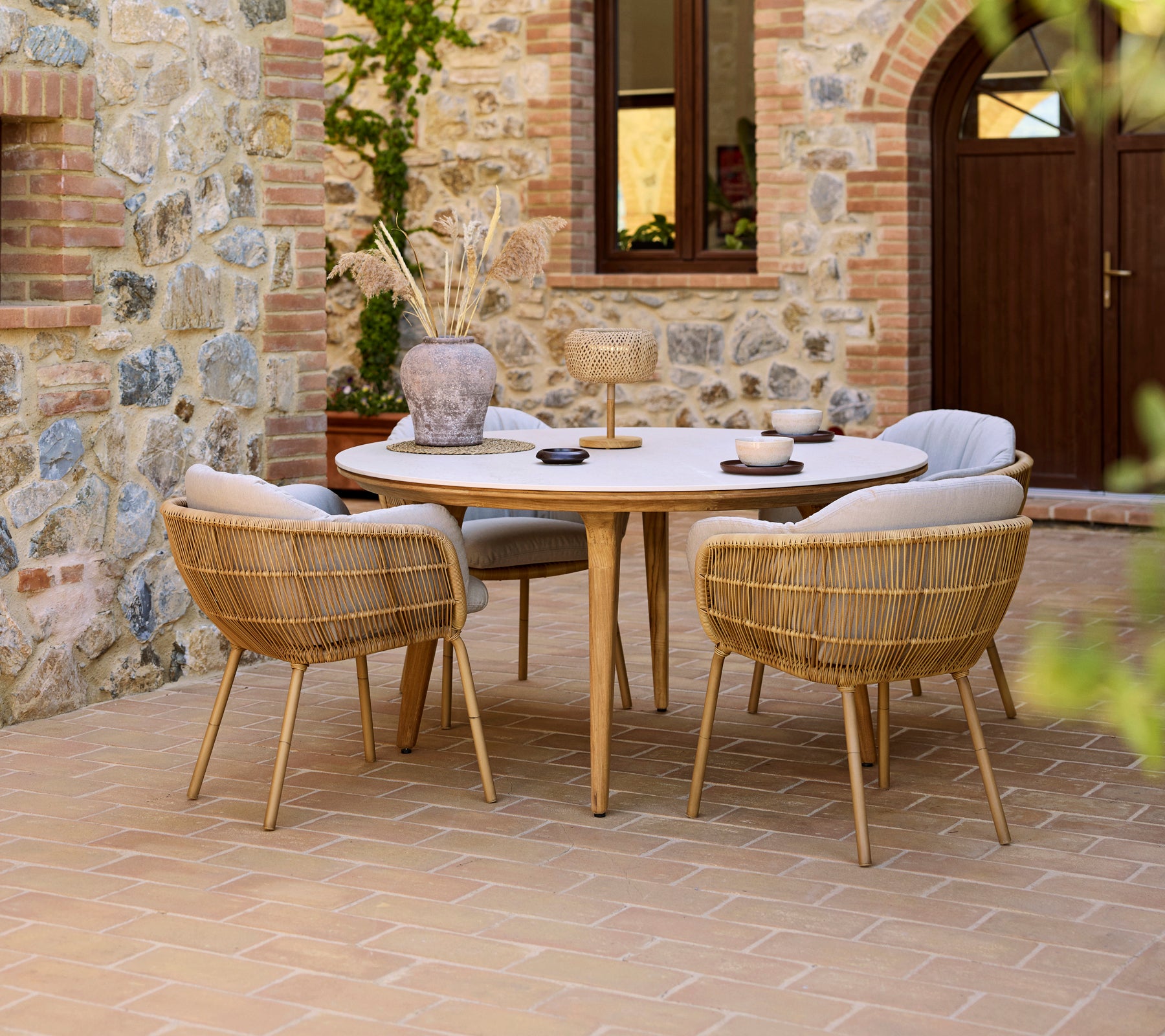 Aménagement de repas en extérieur avec une table Aspect ronde et des chaises Stay, le tout devant un mur en pierre.