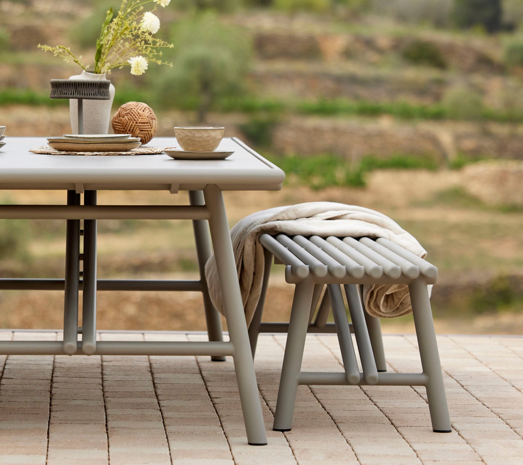 Une mise en place de table élégante avec des bols, des tasses et un centre de table décoratif, accompagnée d'un tabouret assorti de style bâton.