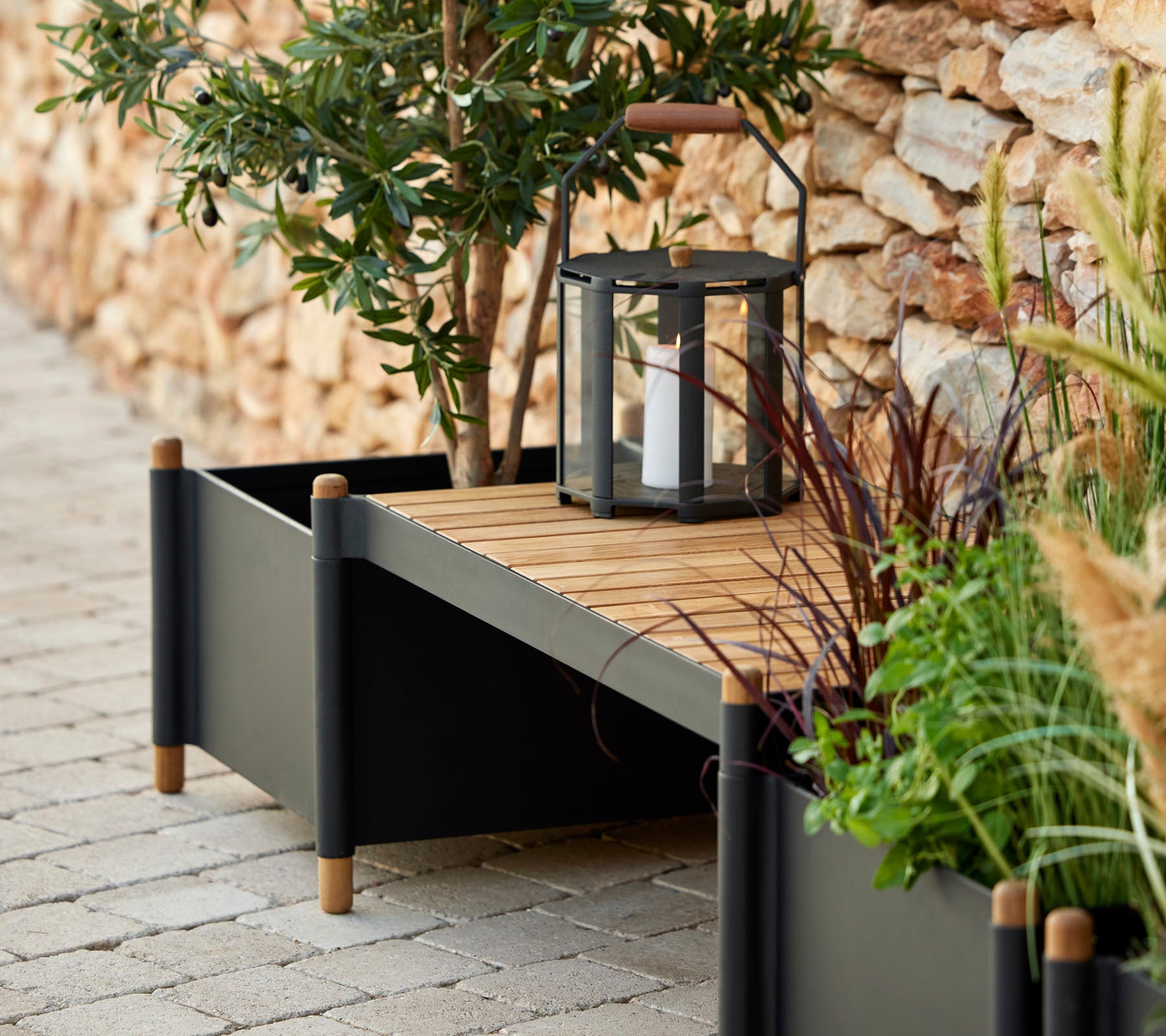 Une jardinière élégante avec des lattes en bois, entourée de verdure et d'une lanterne, ajoutant une touche d'élégance à l'espace.