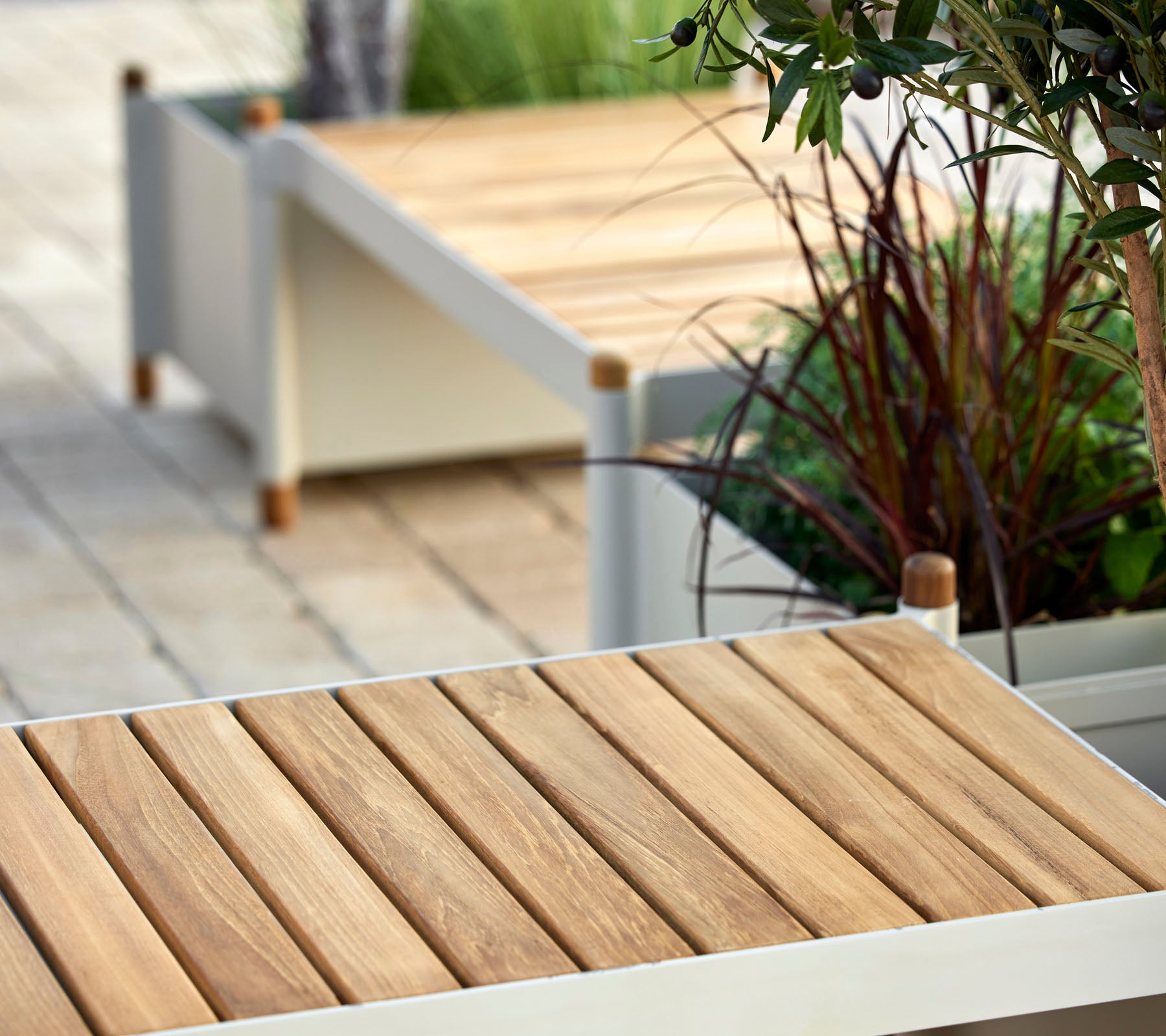 Surface en lattes de bois avec des éléments de design minimalistes, entourée de verdure et de jardinières décoratives.