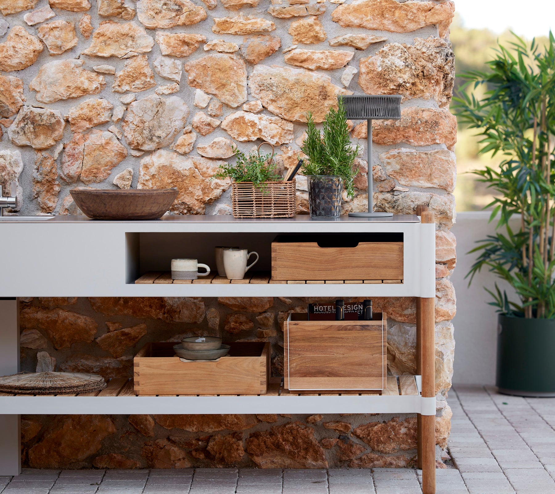 Aménagement de cuisine élégant avec un mur en pierre, des boîtes de rangement en bois, des plantes en pot et une lampe illusion pour une atmosphère accueillante.