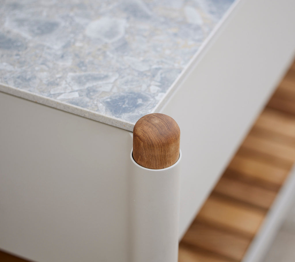 Détail d'angle en bois d'un meuble avec une surface texturée et des supports verticaux, soulignant une esthétique moderne.
