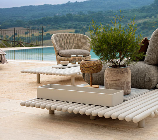 Mobilier d'extérieur élégant avec des bâtons en aluminium, un pot de fleurs rond et des éléments décoratifs, dans un paysage serein.